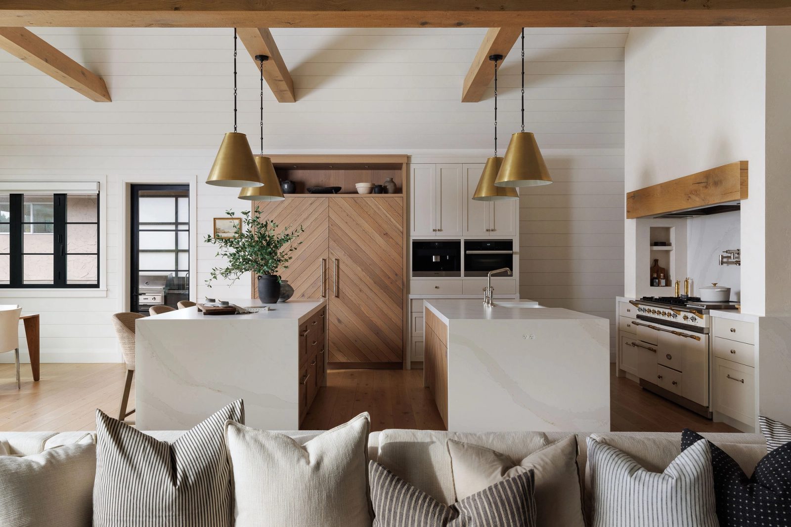 Kitchen and living space under exposed beams, with a chevron oak pantry wall and twin stone islands