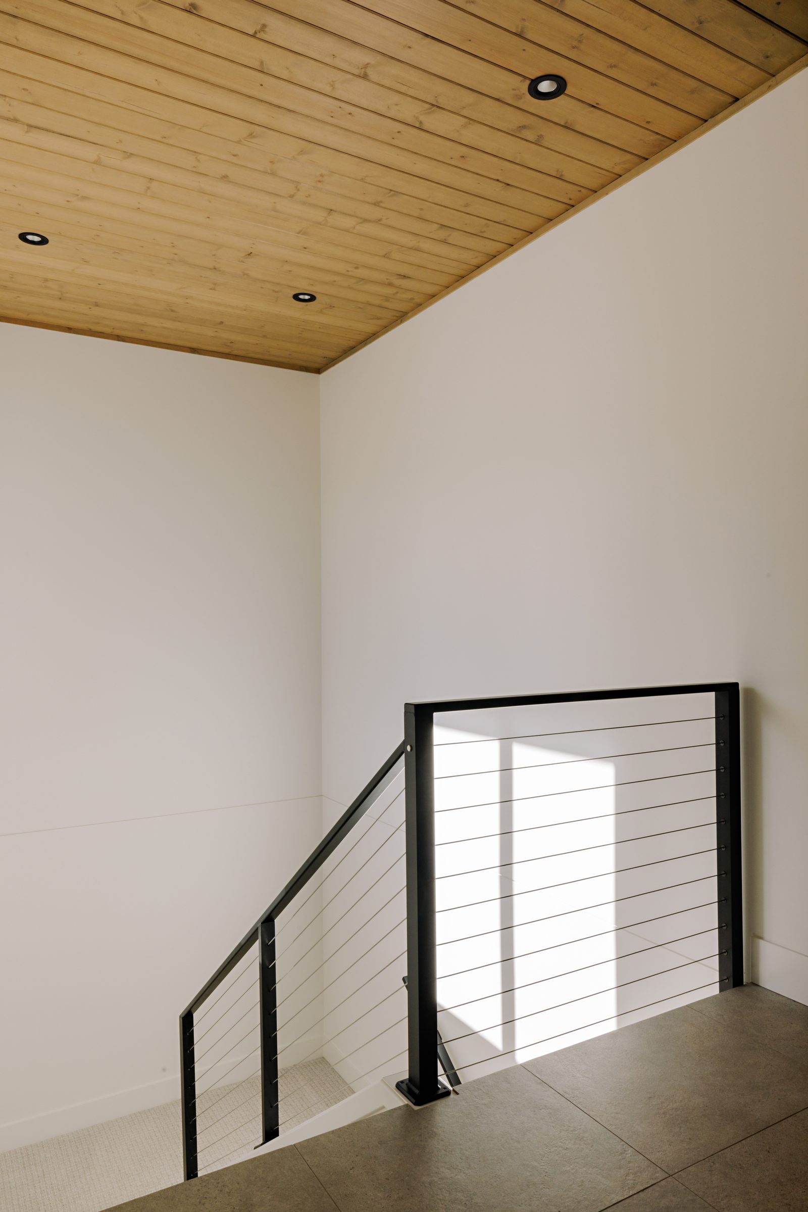 the same rail from above, looking down the flight into shadow, sunlight falling in a hard rectangle on the wall.