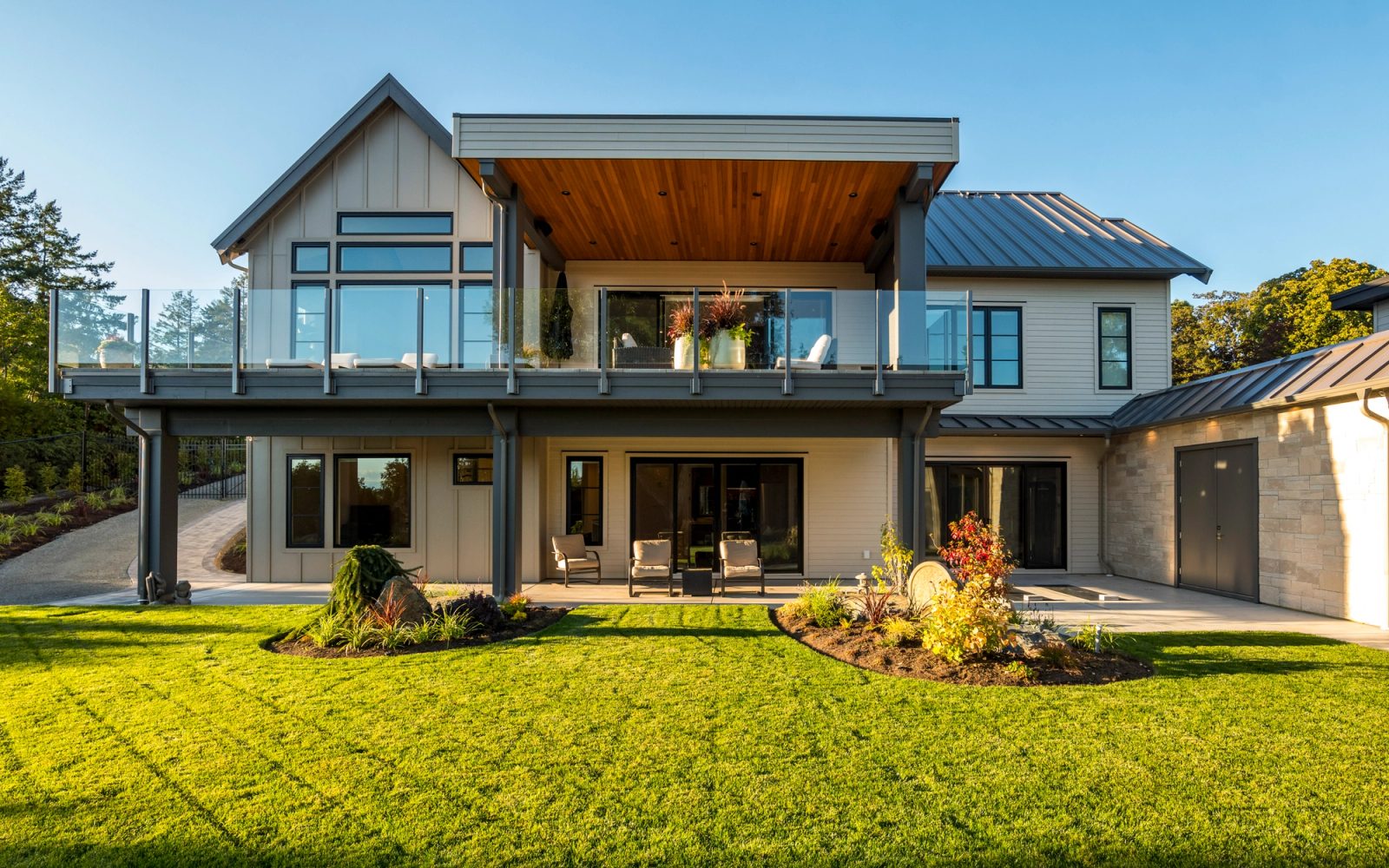 Rear elevation at golden hour with a glass-railed deck above a covered walk-out patio, facing a level lawn