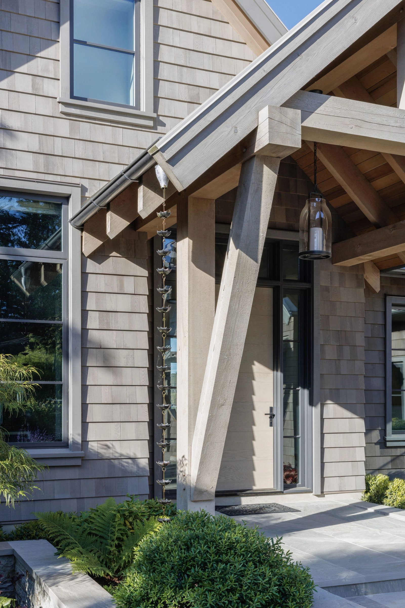 Close view of the entry porch where a timber post and brace meet the beam, a rain chain alongside