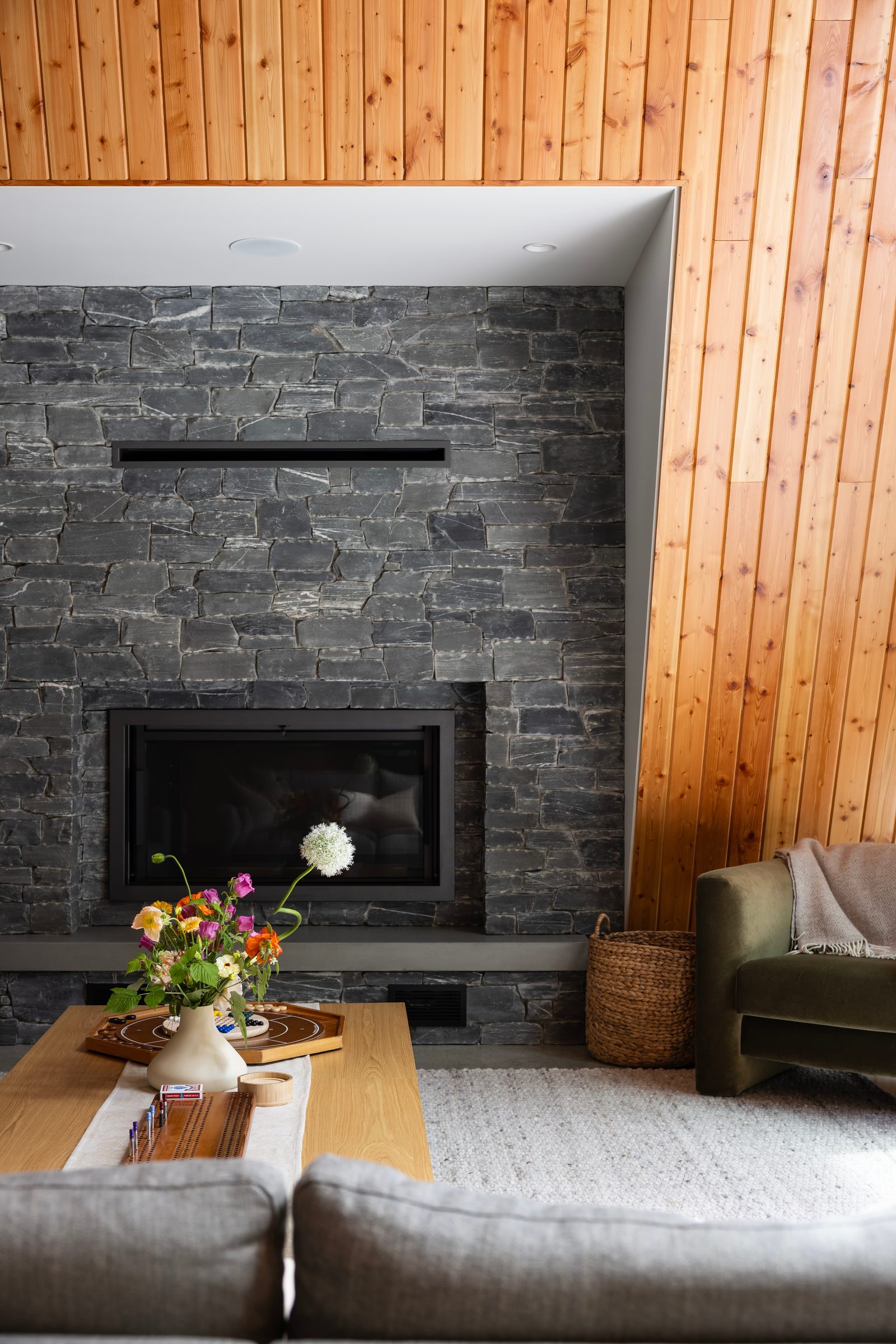 Grey stone fireplace wall meeting vertical cedar panelling