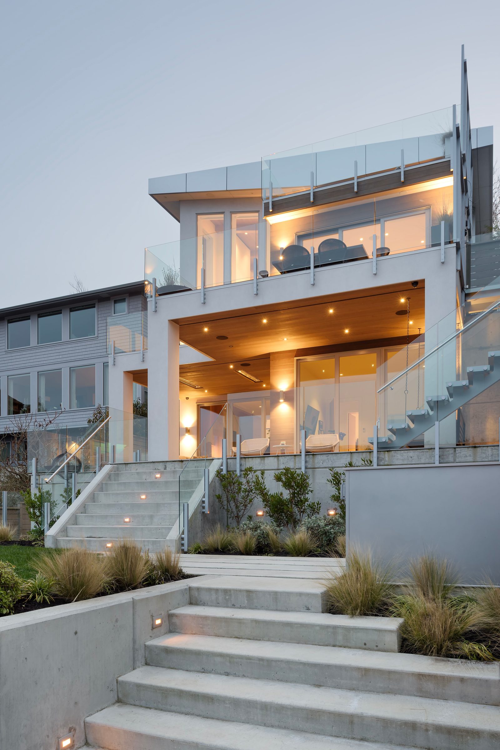 Broad concrete steps climbing between planted grasses to a covered terrace lit from above.