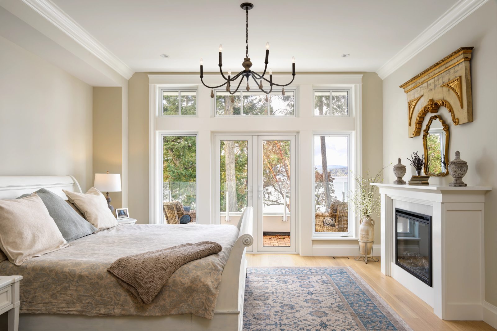 Bedroom with a white sleigh bed, a gilded overmantel mirror, and glazed doors opening to a balcony above the water.