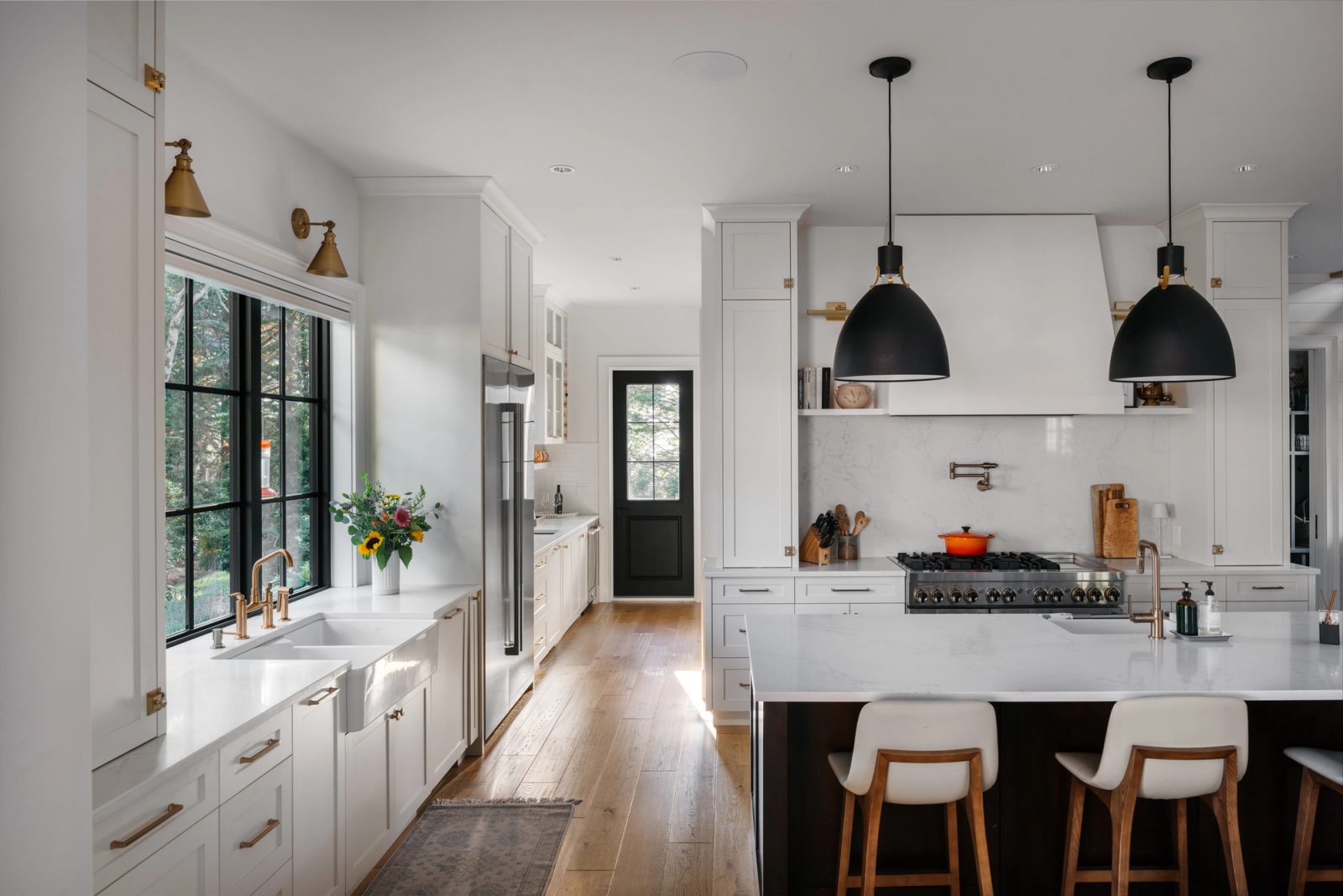 Kitchen with a white plaster hood, marble-look quartz island and a farmhouse sink set under black steel windows