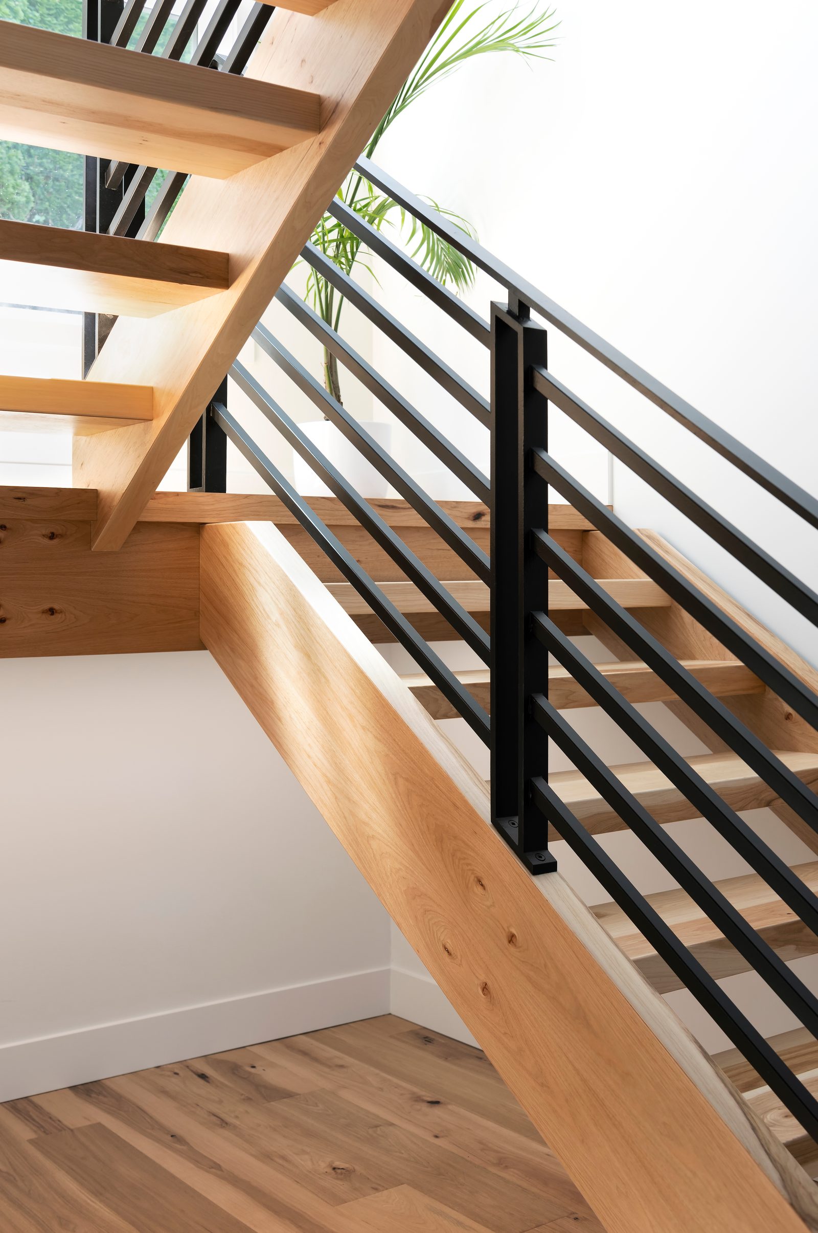 Hickory stair treads cantilevered from a solid stringer, seen from below with a black steel rail beyond