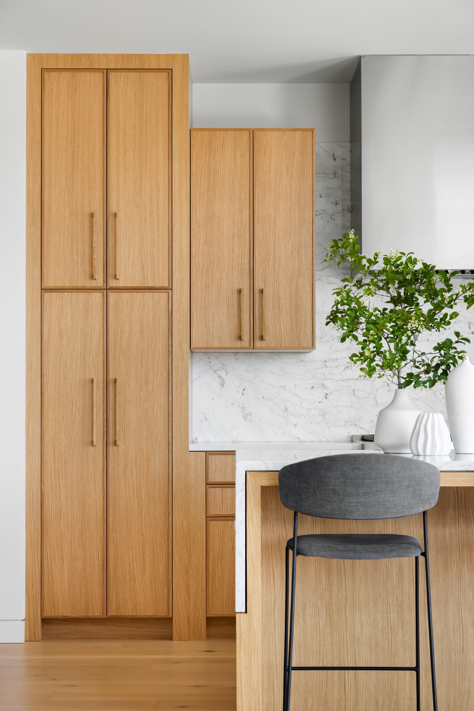 Tall oak pantry doors beside the island, with a branch in a white vase on the counter.