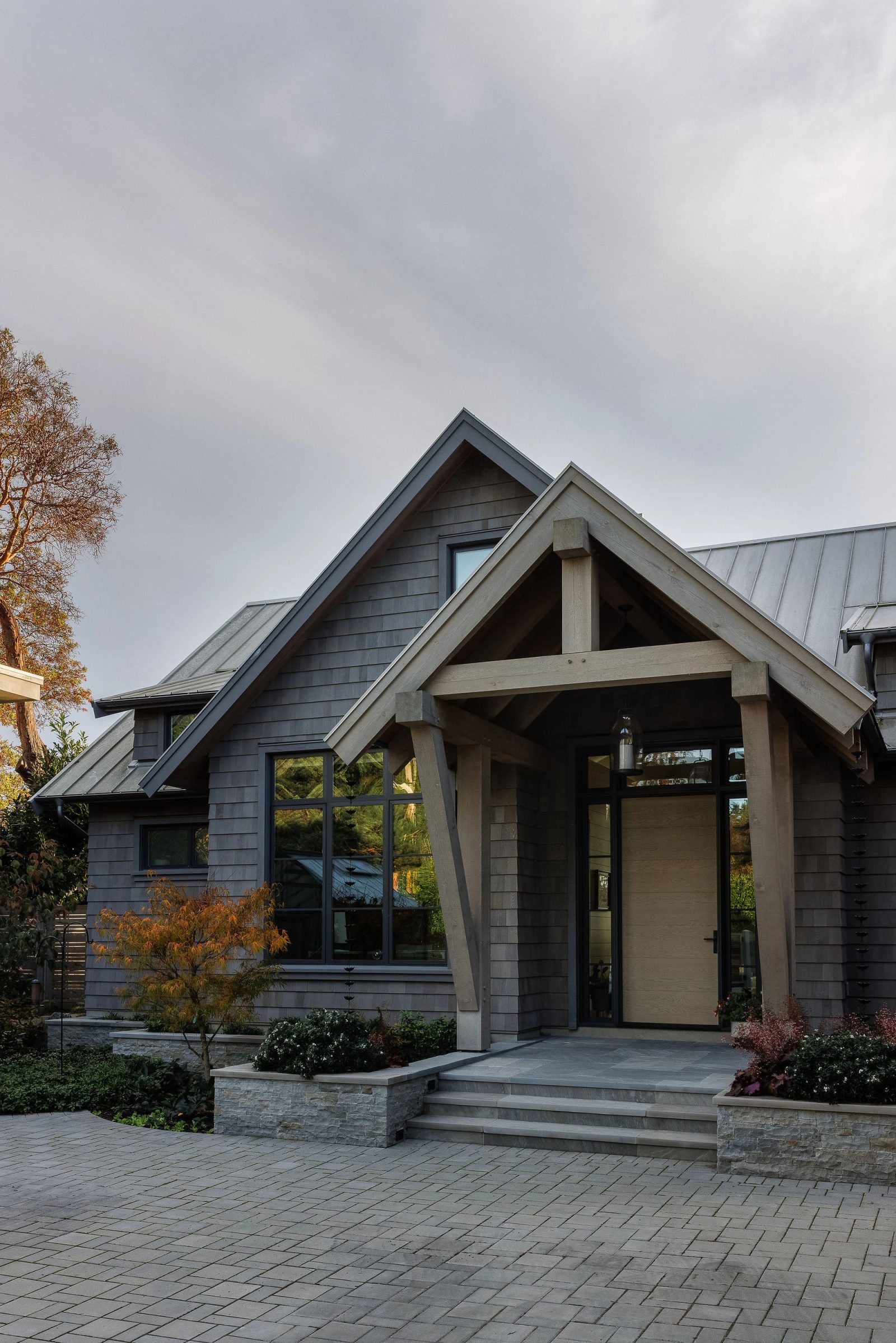 The timber-truss entry porch and oak door at dusk, seen across the paved courtyard