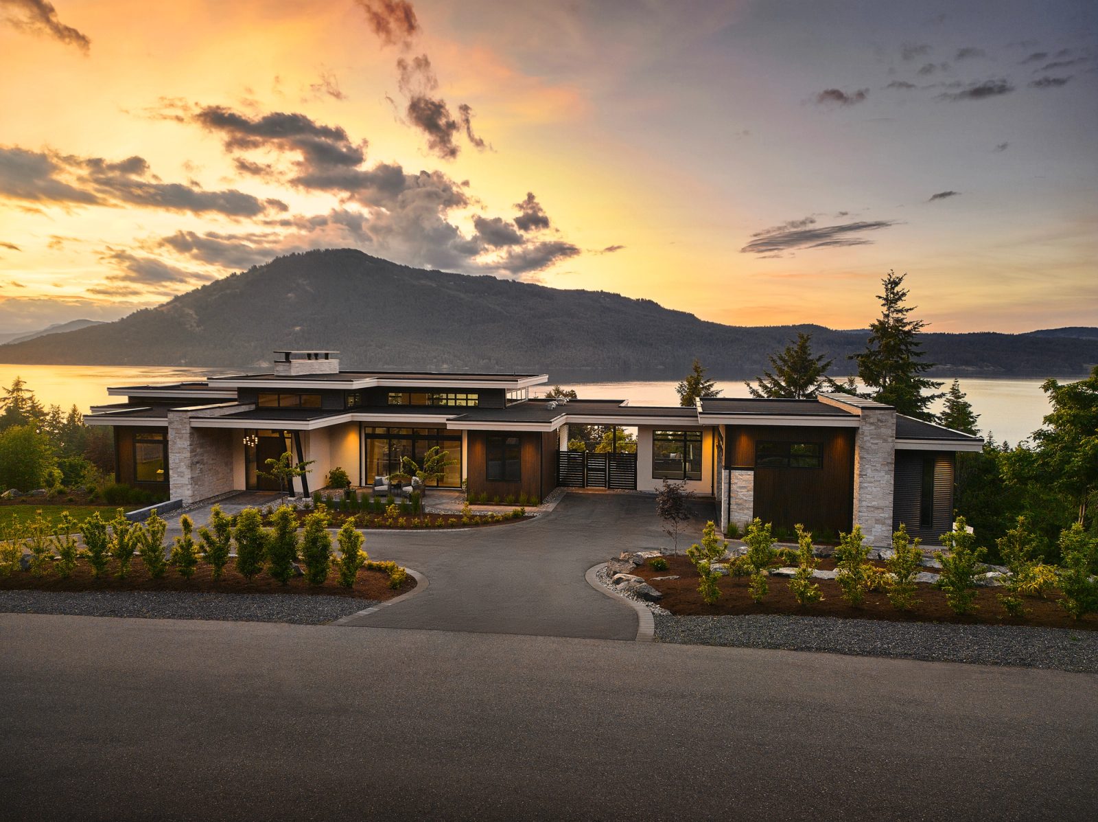 Low flat-roofed house at sunset in North Saanich, stone piers and dark siding, Mt Tuam beyond