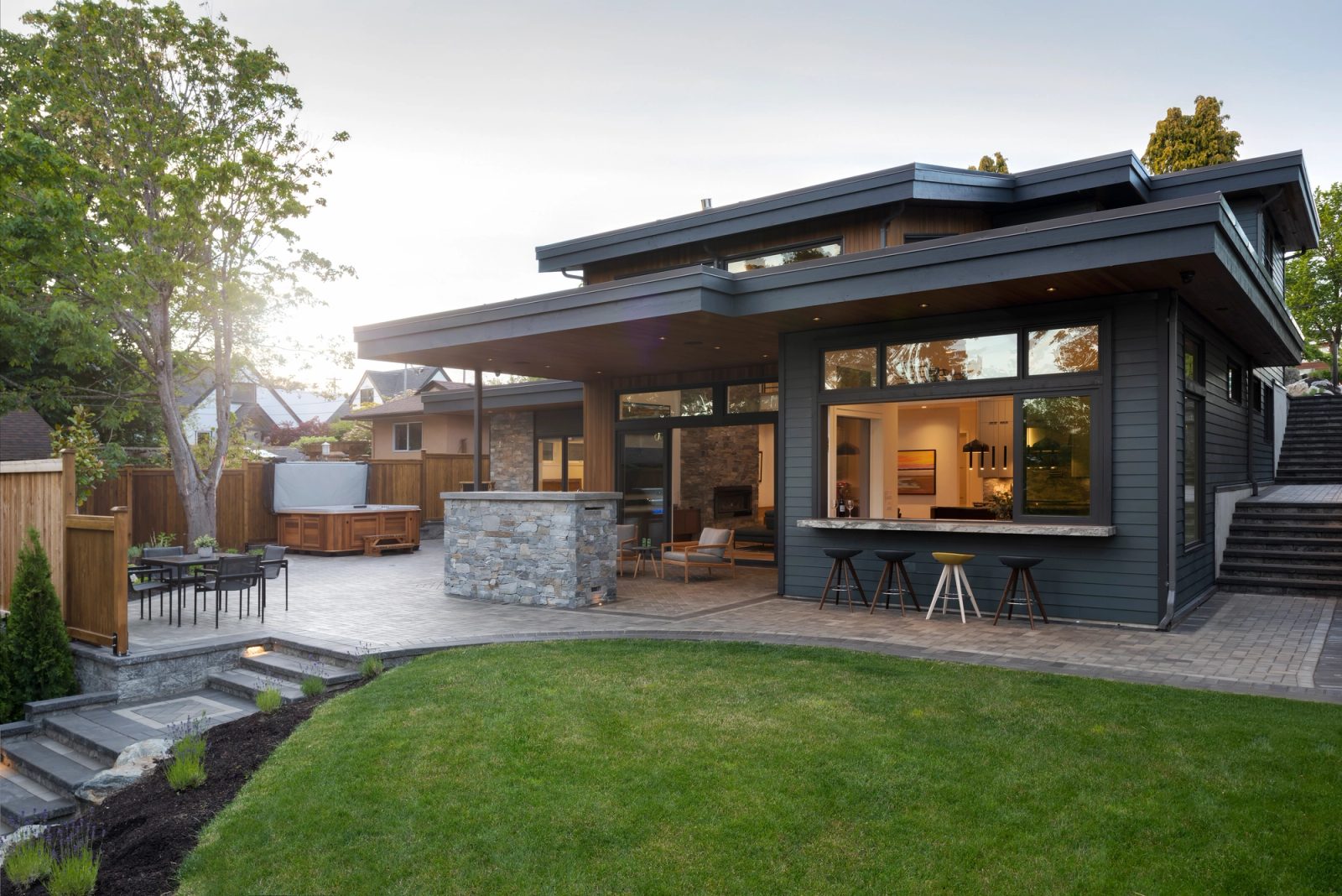 Rear elevation with deep flat roof overhangs, a covered patio and a stone bar counter facing a curved lawn