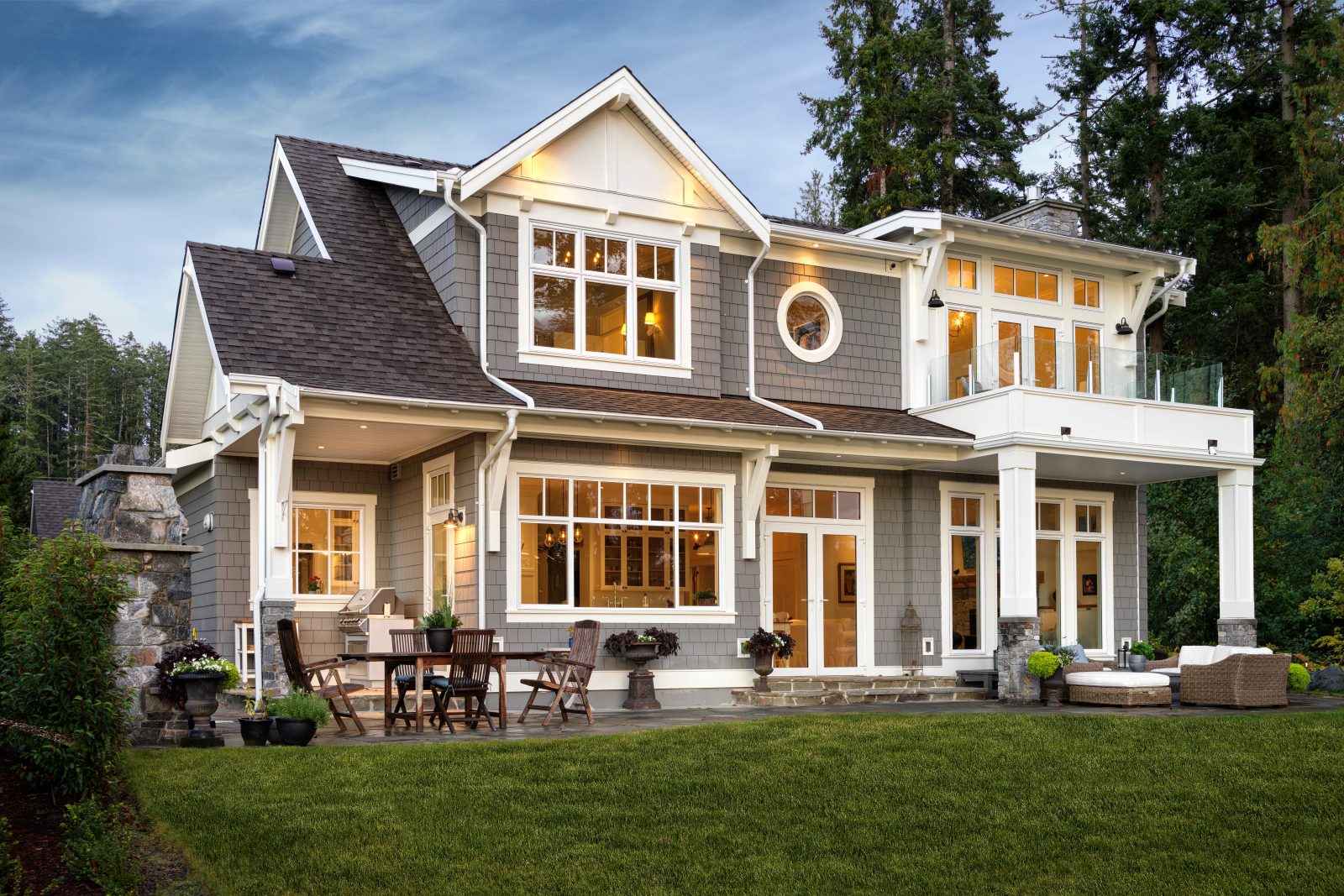 Rear elevation at dusk, shingled with white trim, a covered porch below and a glass-railed deck above, seen across a lawn.