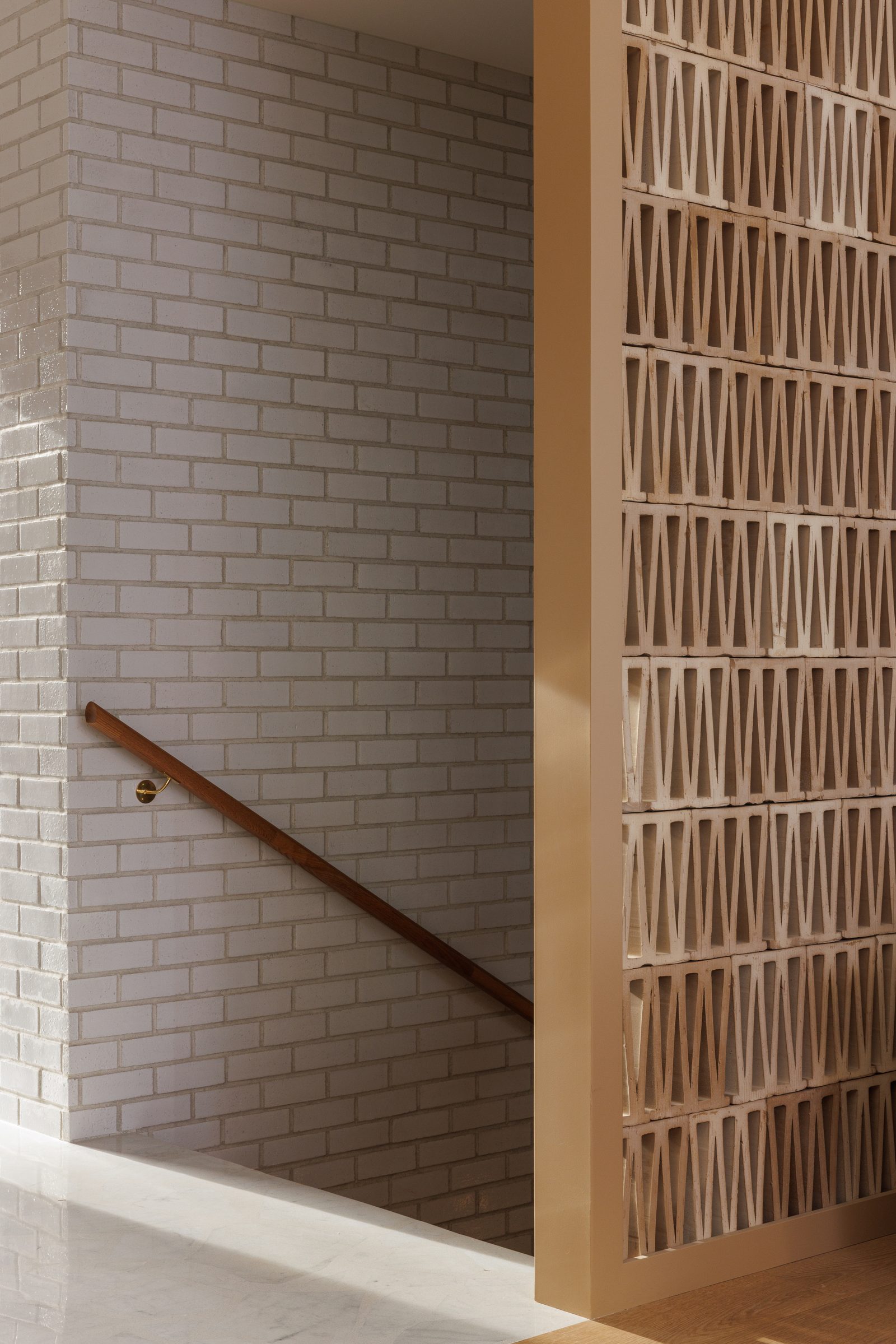 Right: an oak handrail on brass brackets running down a wall of glazed white brick, the same block screen alongside in raking light.