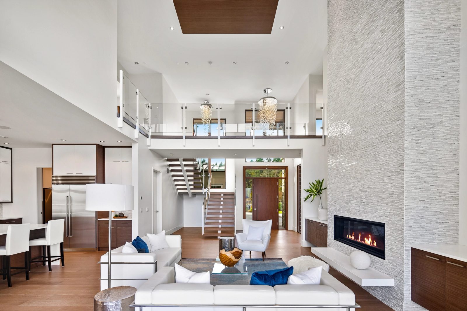 Living room looking back to a floating stair, glass-railed upper gallery and walnut entry door