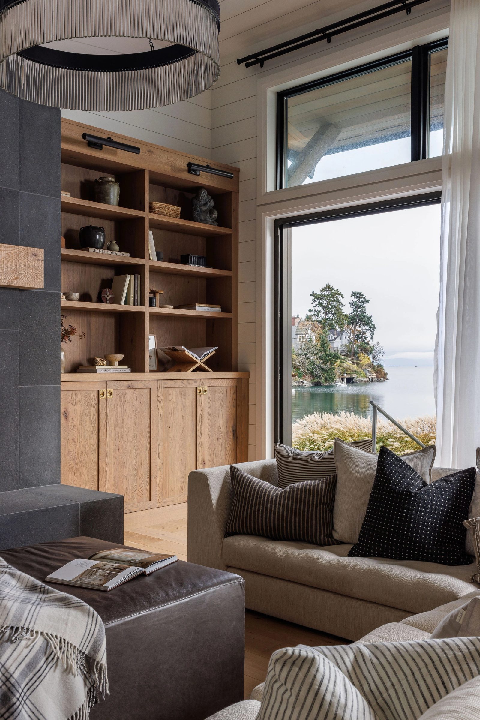 Living room with oak built-ins beside a tall window looking across the bay to the far shore