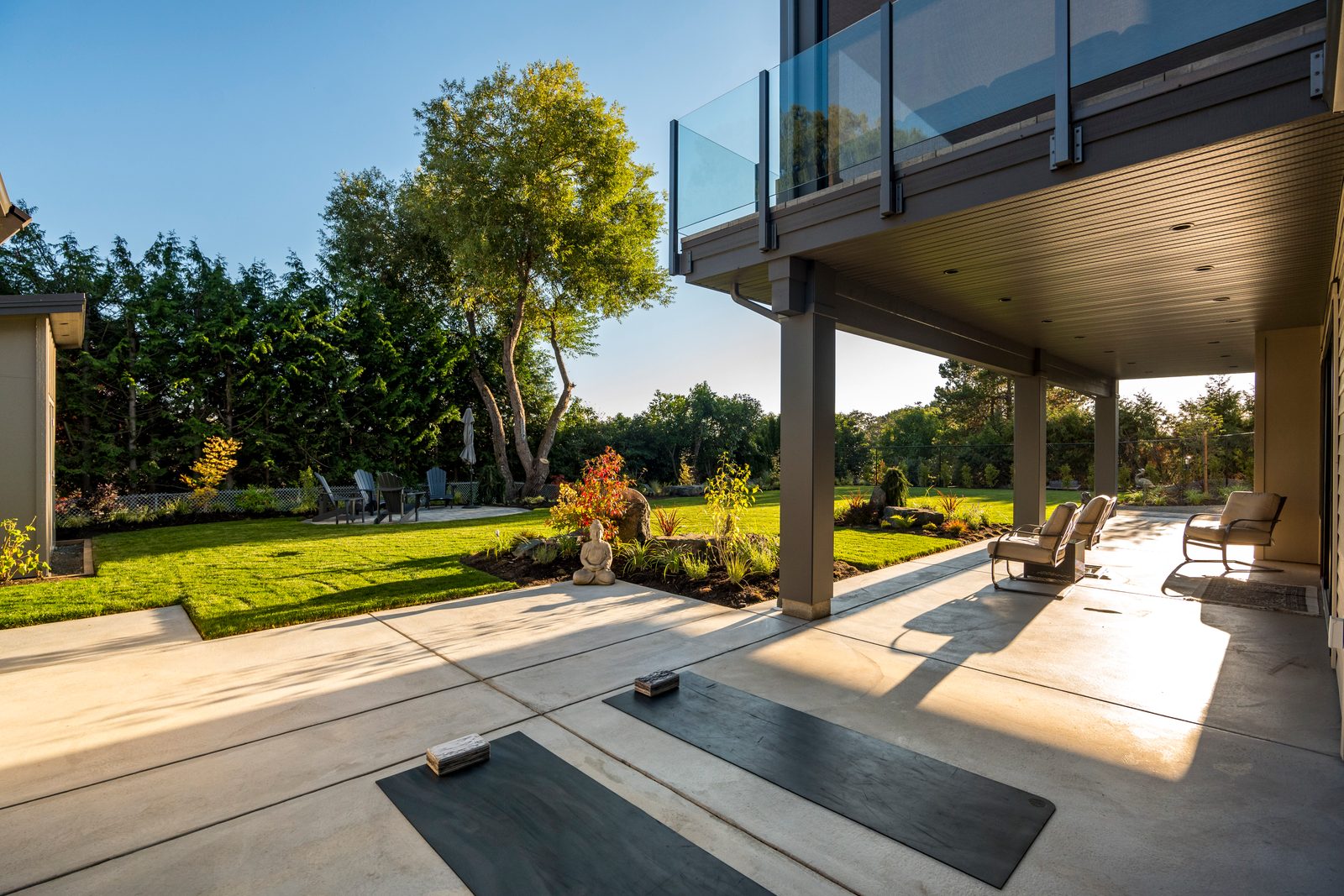 Covered walk-out terrace with exercise mats under a glass-railed deck, facing a level lawn