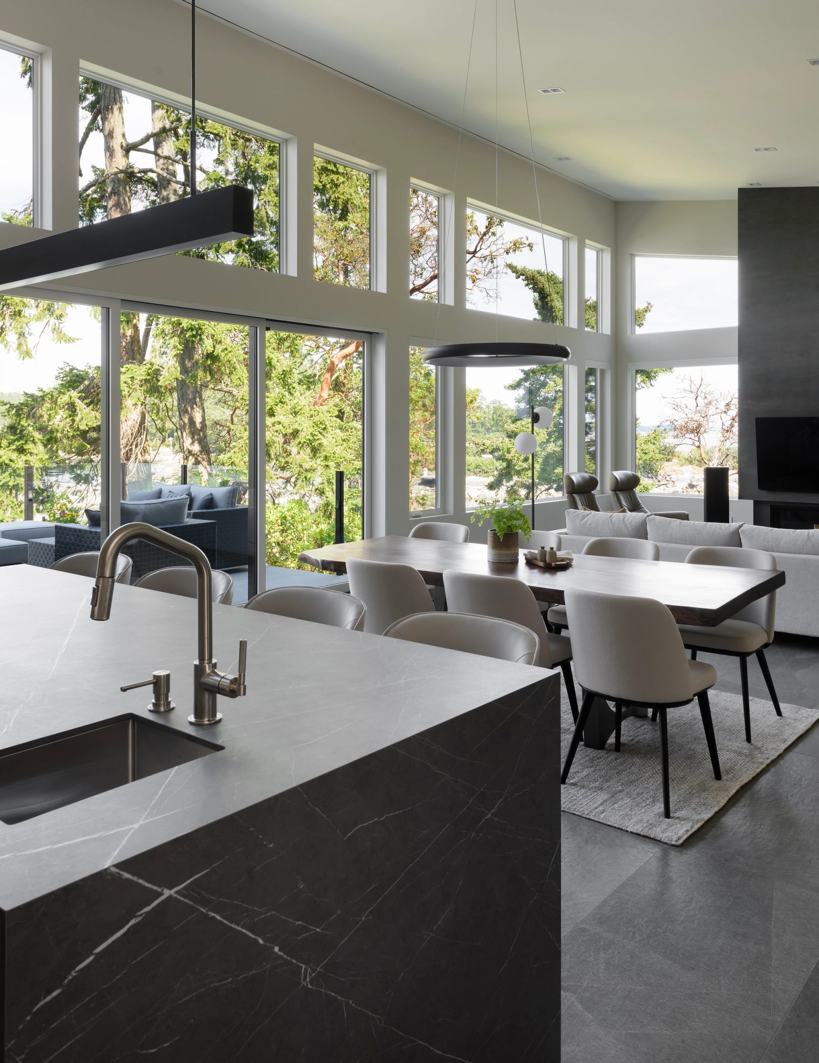 Kitchen island in dark veined stone with a walnut dining table and clerestory glazing above