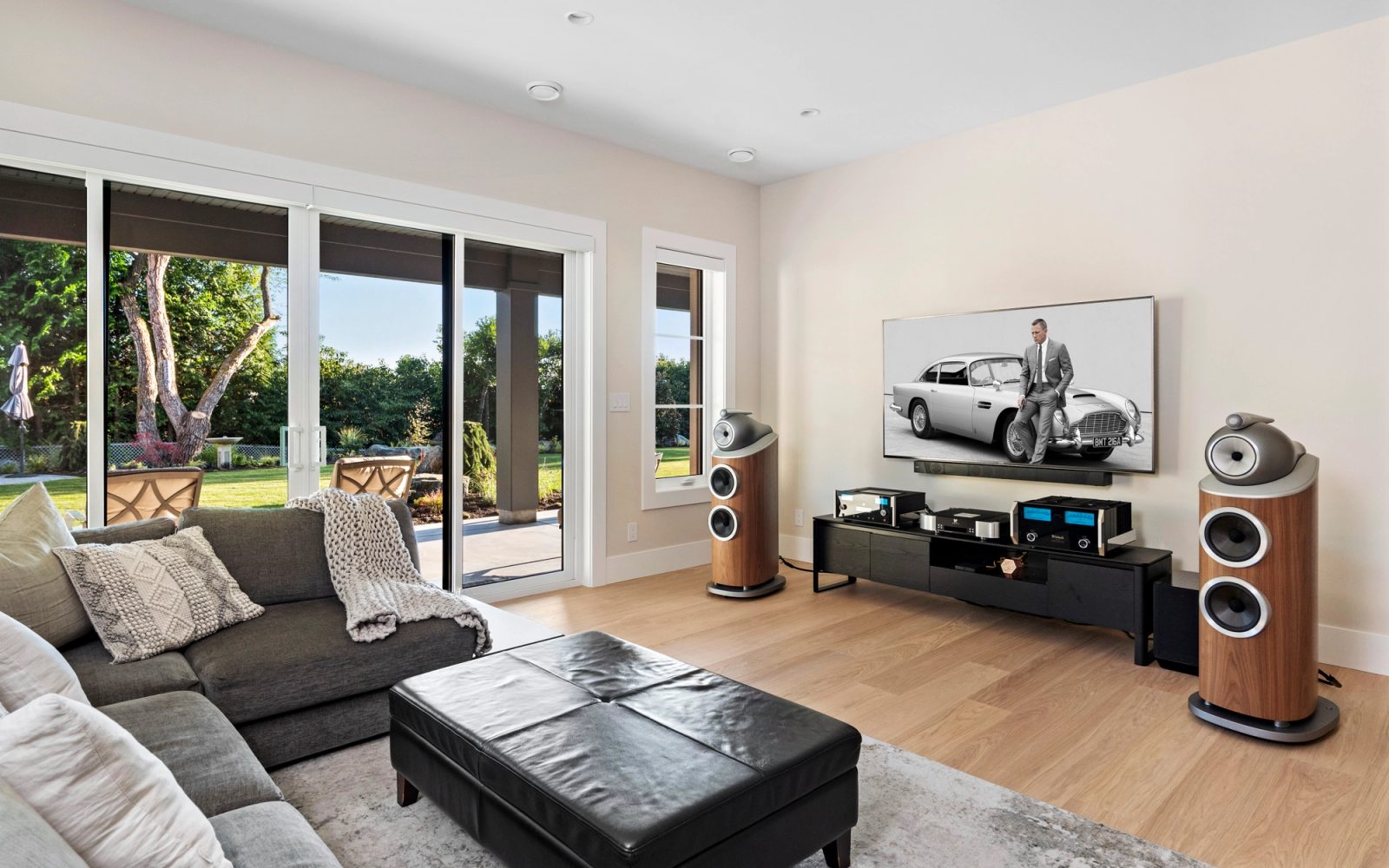 Lower-floor media room with floorstanding speakers and sliding doors to the lawn