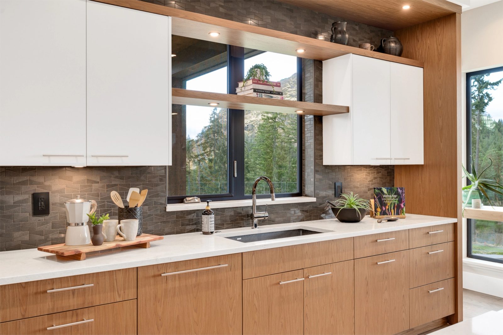 Kitchen sink run in rift white oak with a graphite chevron tile backsplash and a window framing the rock bluff
