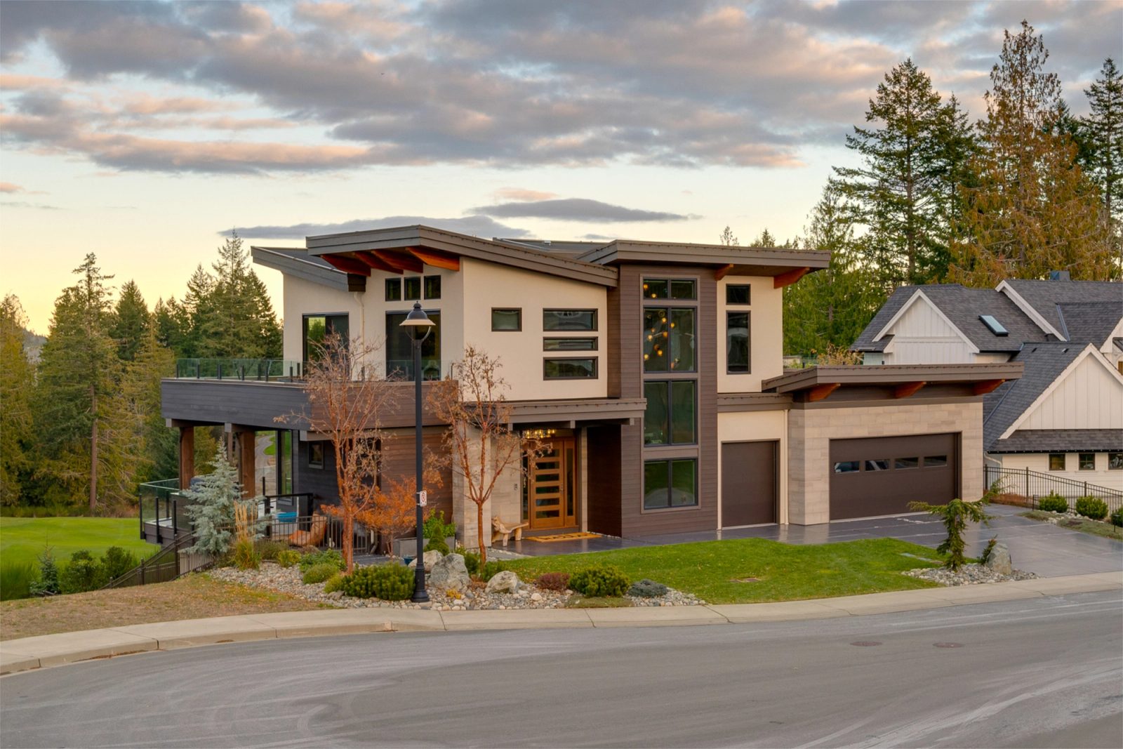 Contemporary house seen from the corner at dusk, stepping down the slope to a lower terrace above the fairway