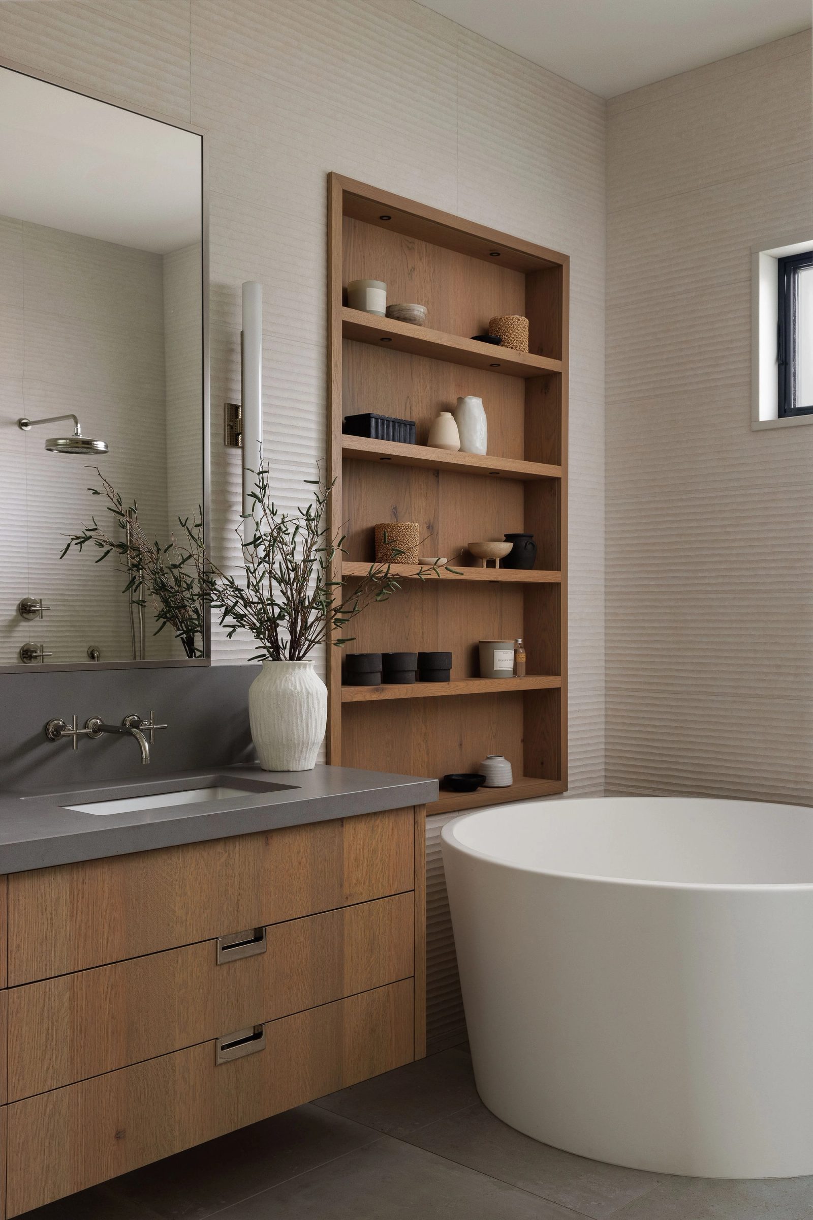 Primary bathroom with a round soaking tub, oak vanity and recessed oak shelving