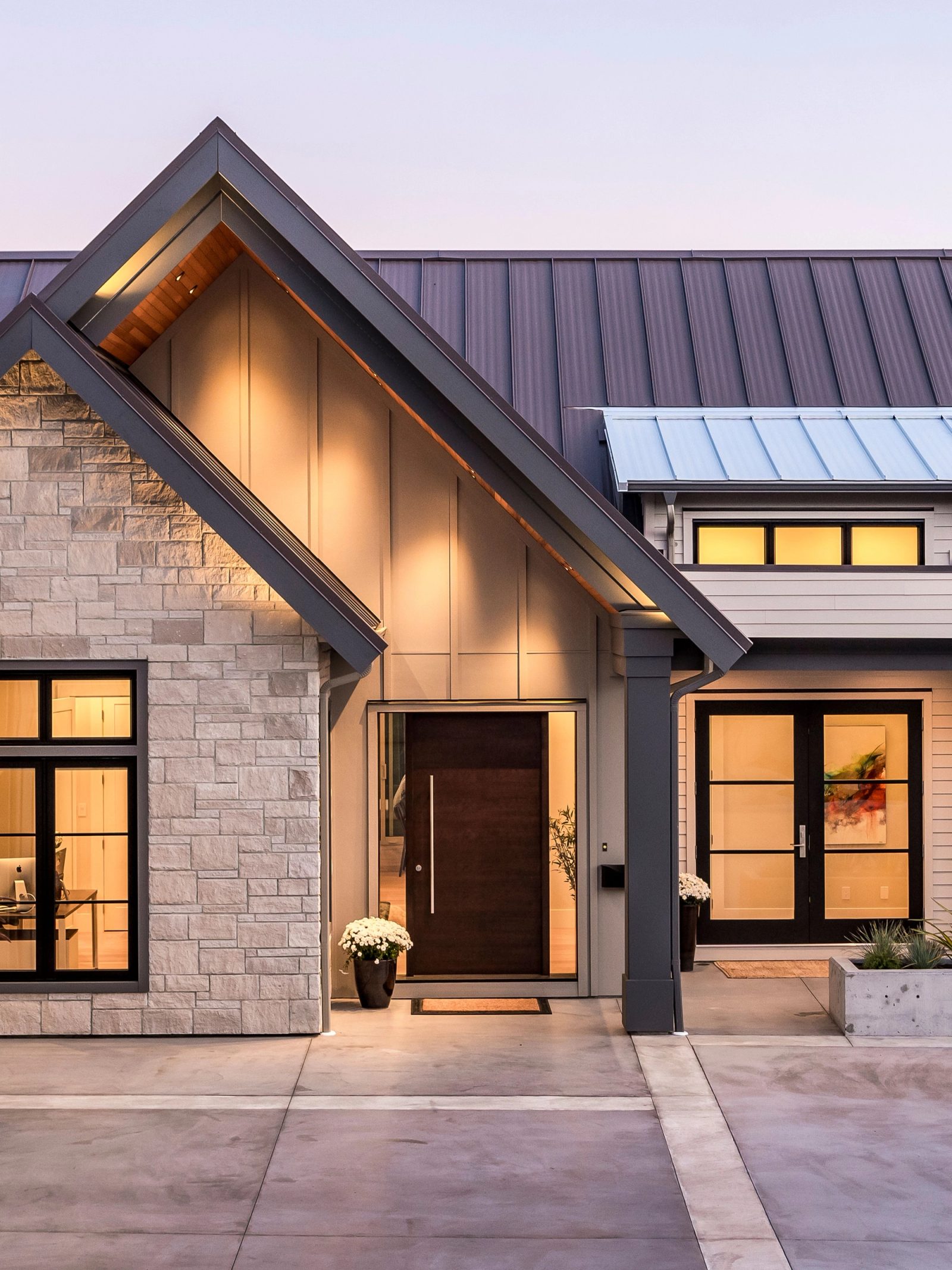 Gabled entry at dusk with a lit cedar soffit, a walnut front door and stone flanking the office window