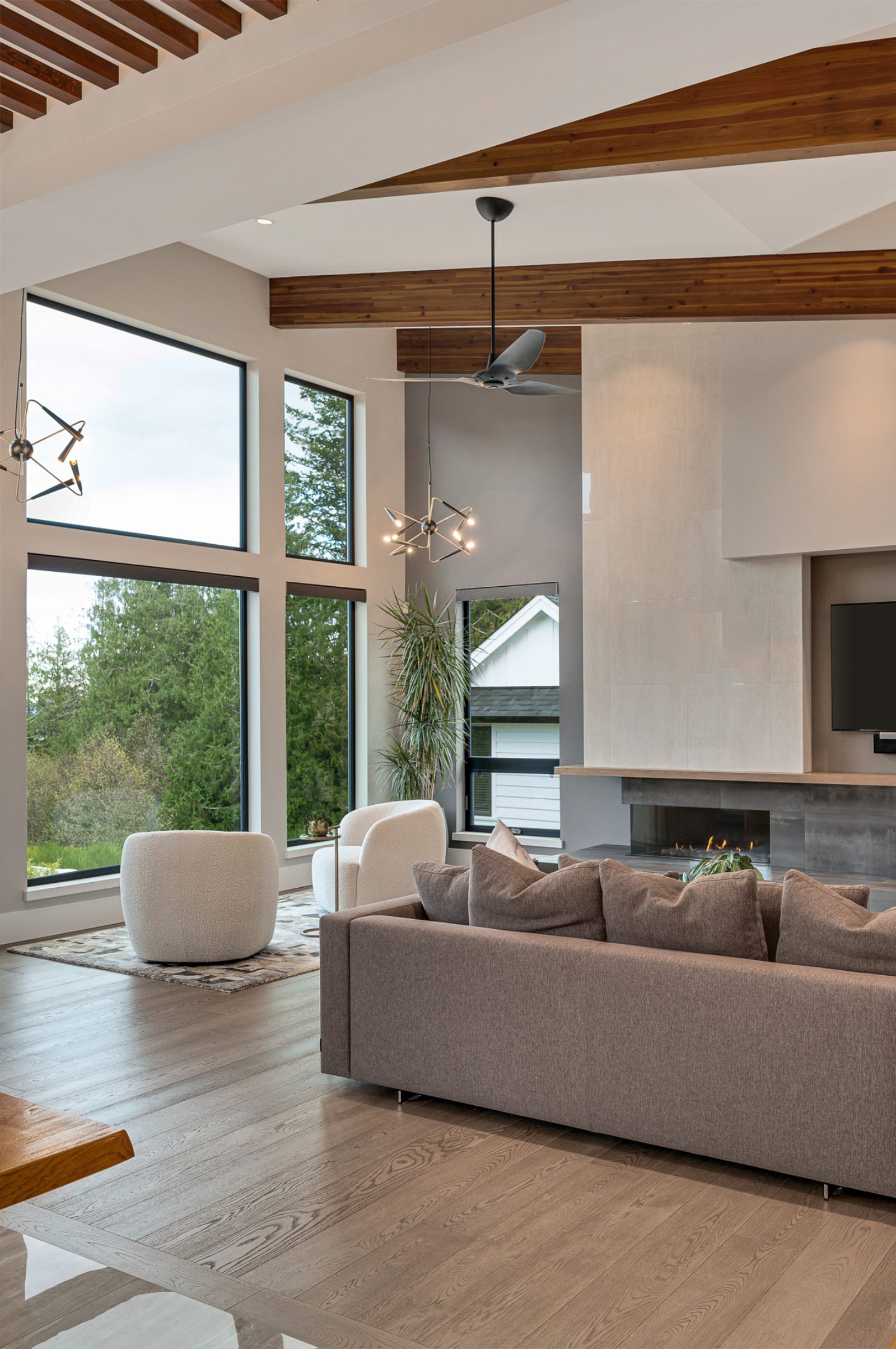 Living room under a cedar ridge beam, with boucle chairs turned toward a two-storey corner window