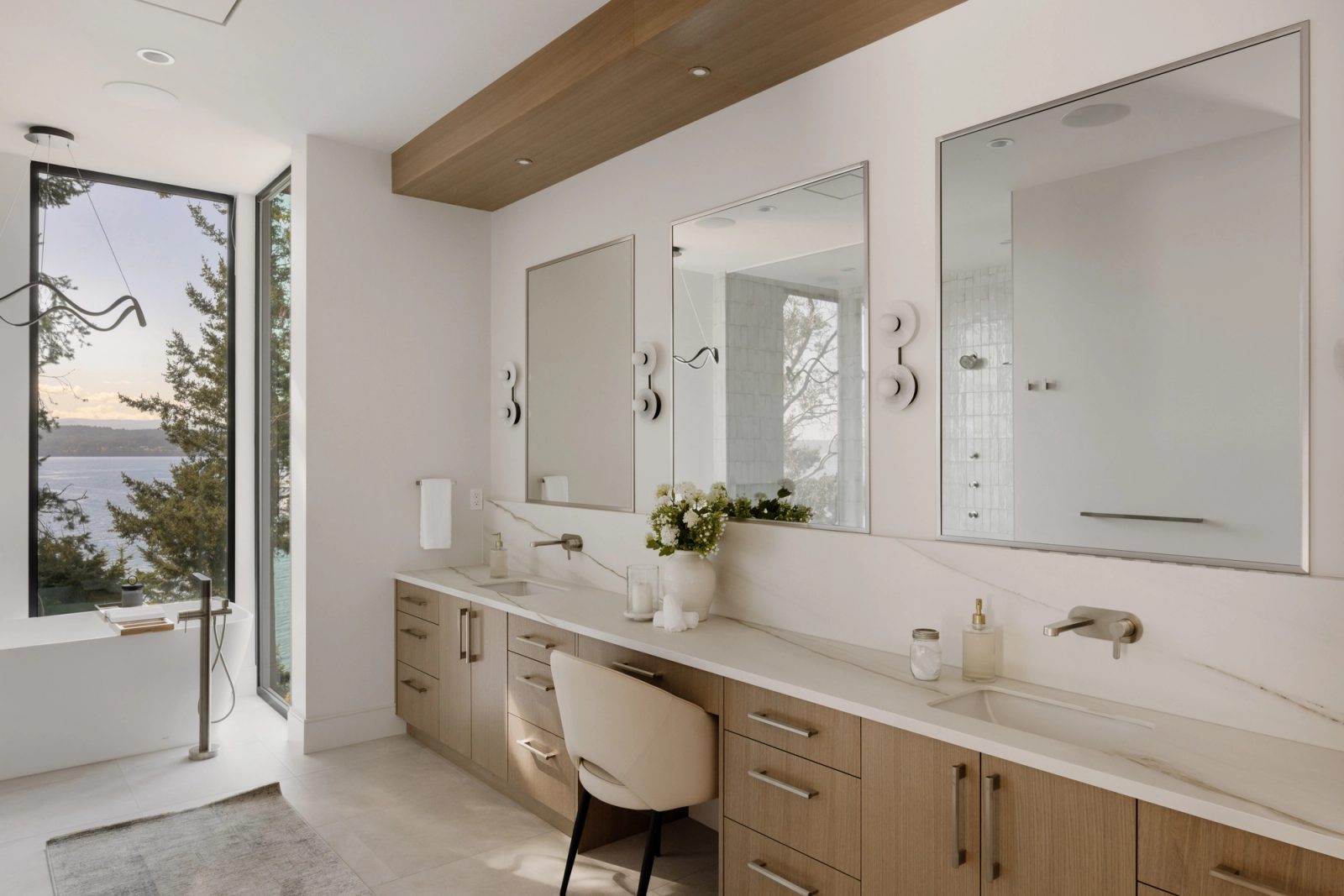 A bathroom with a freestanding tub set into a corner window above the water, and a long marble counter with three mirrors opposite.