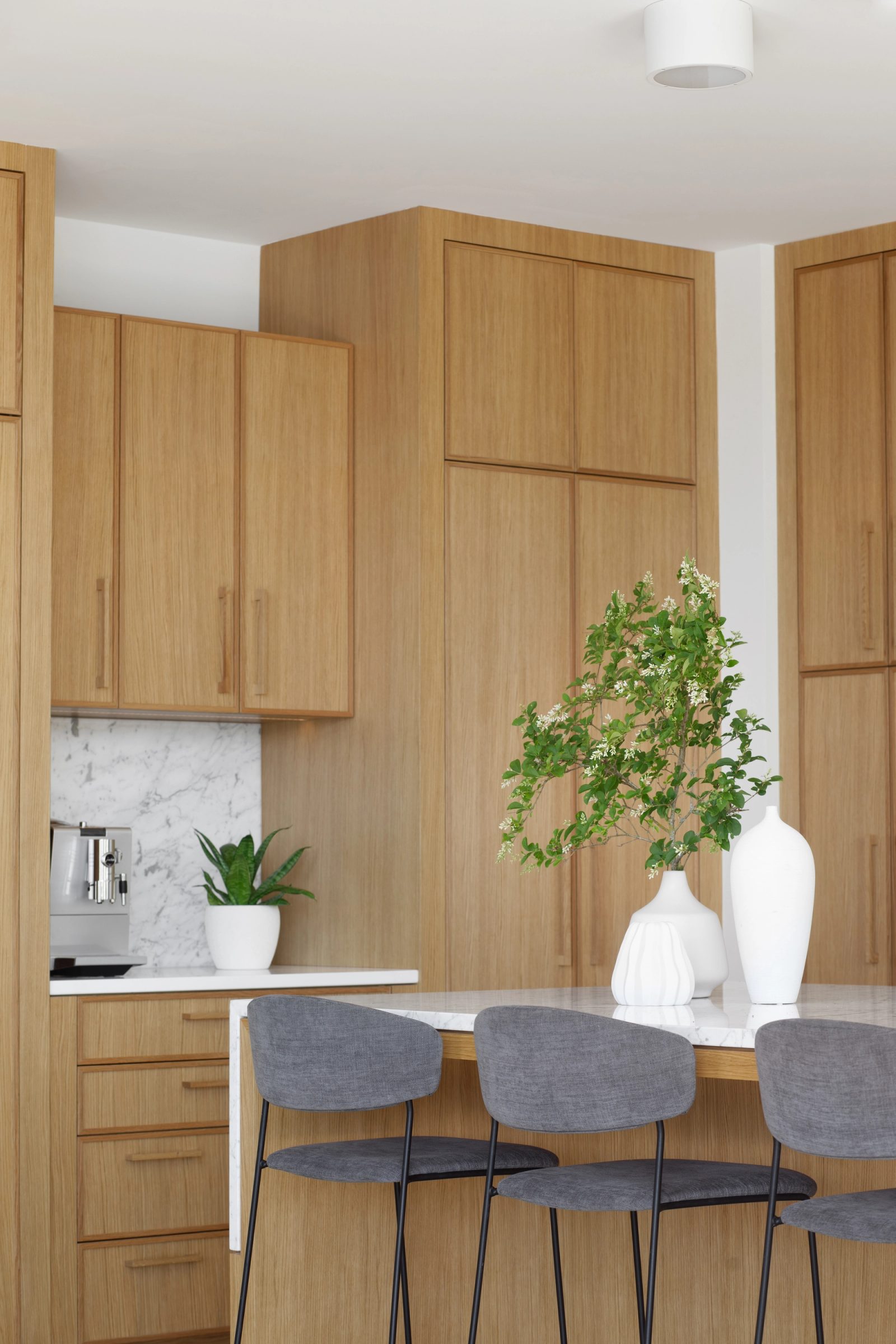 Marble-topped island with stools, seen against a run of full-height oak cabinets and a coffee station beyond.