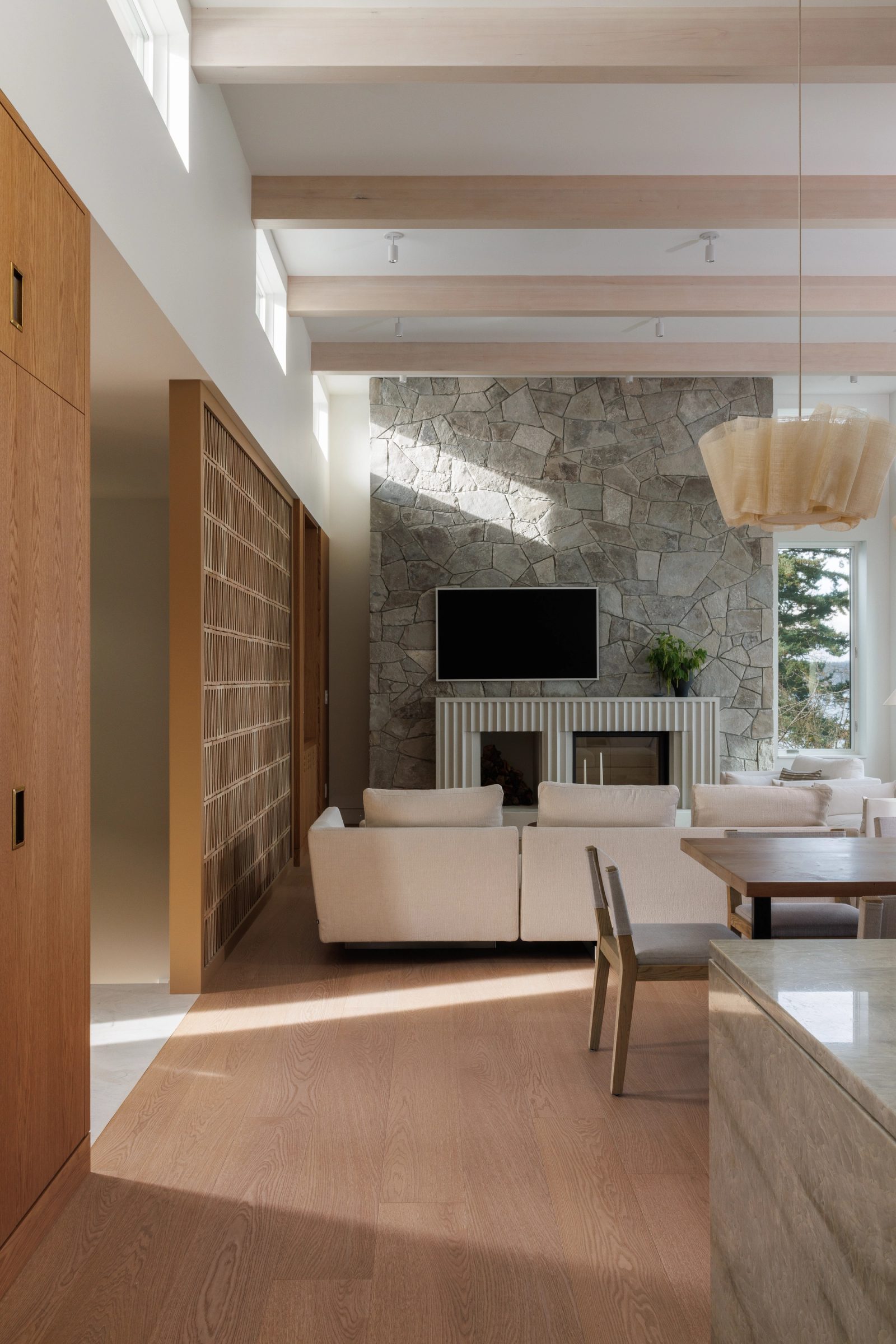 Left: an open living and dining room under whitewashed beams, a block screen wall down one side and a stone chimney standing at the far end.