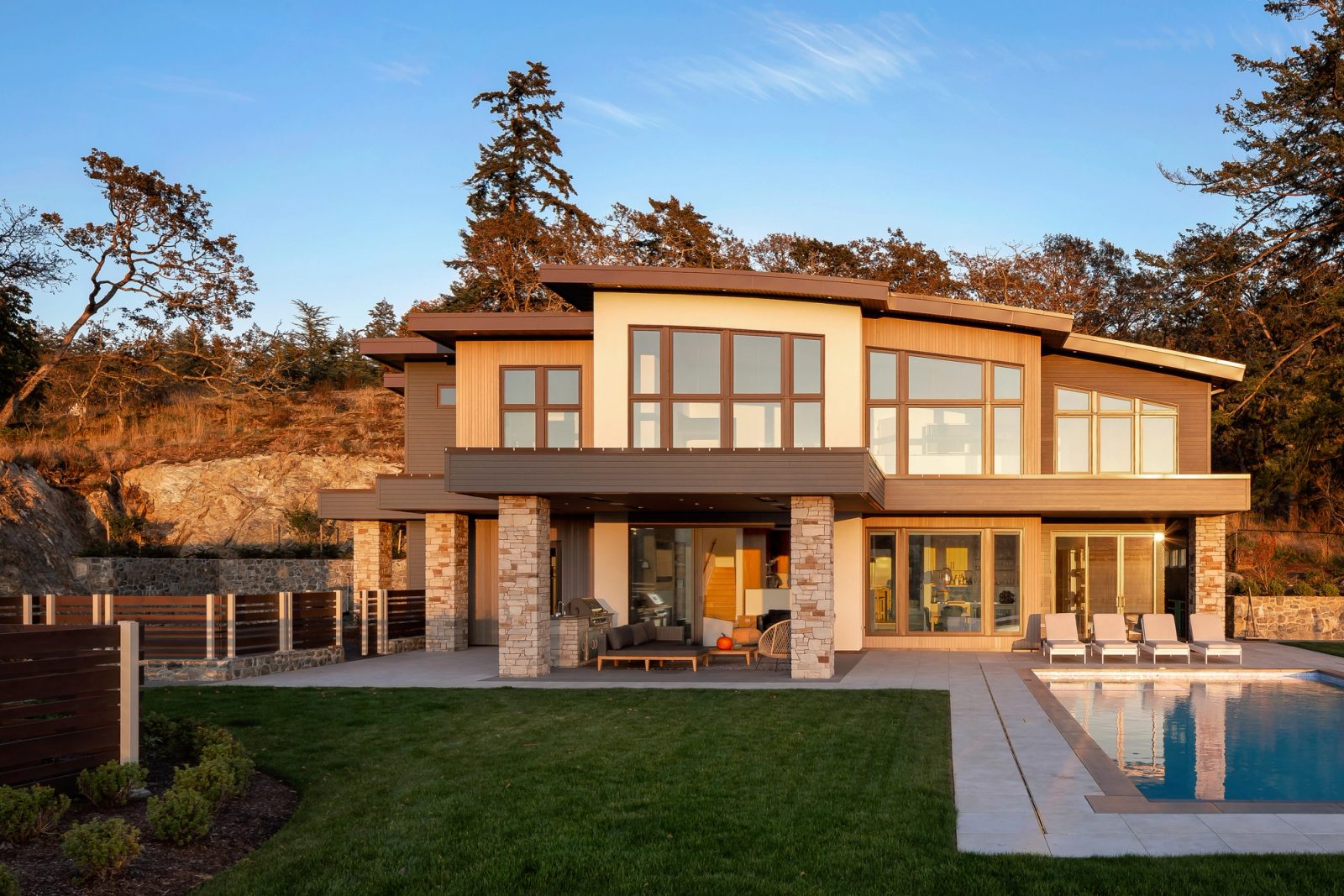 Rear elevation at sunset, upper floor carried on stone piers above a covered terrace and pool