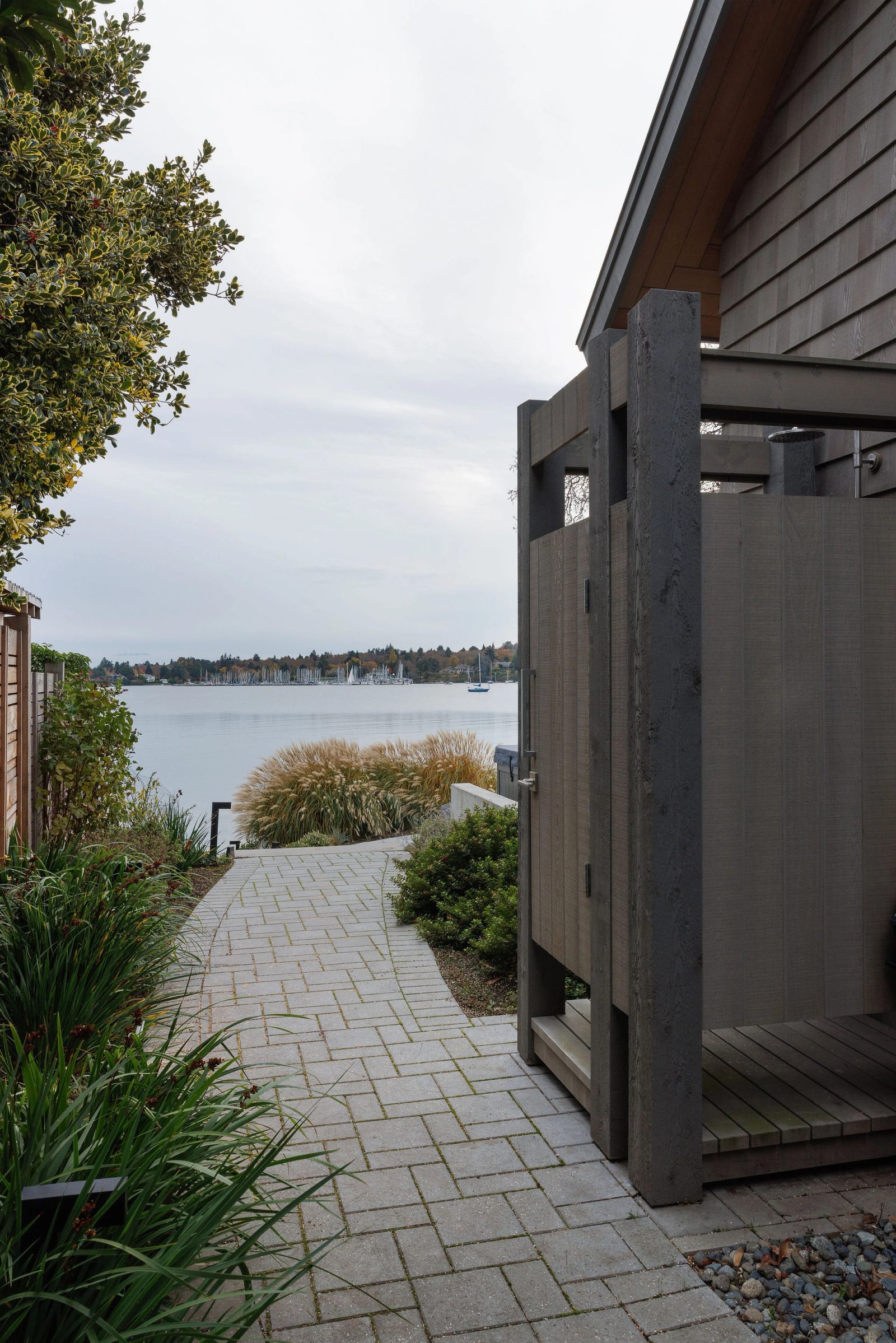 Cedar-screened outdoor shower beside a paved path running down to the bay and the marina beyond