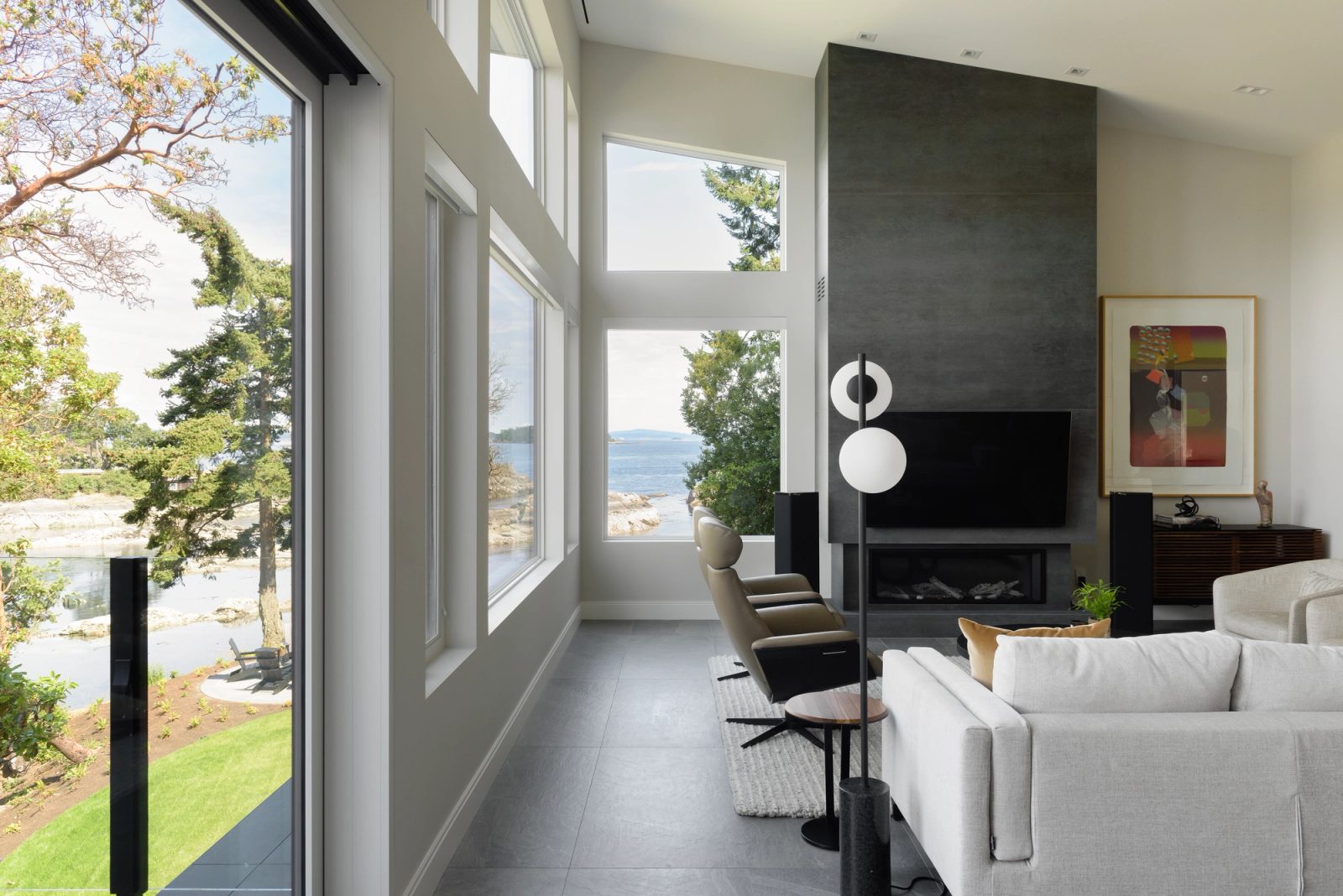 Living room with a full height honed porcelain fireplace wall and corner glazing looking out to islands and a rock shore
