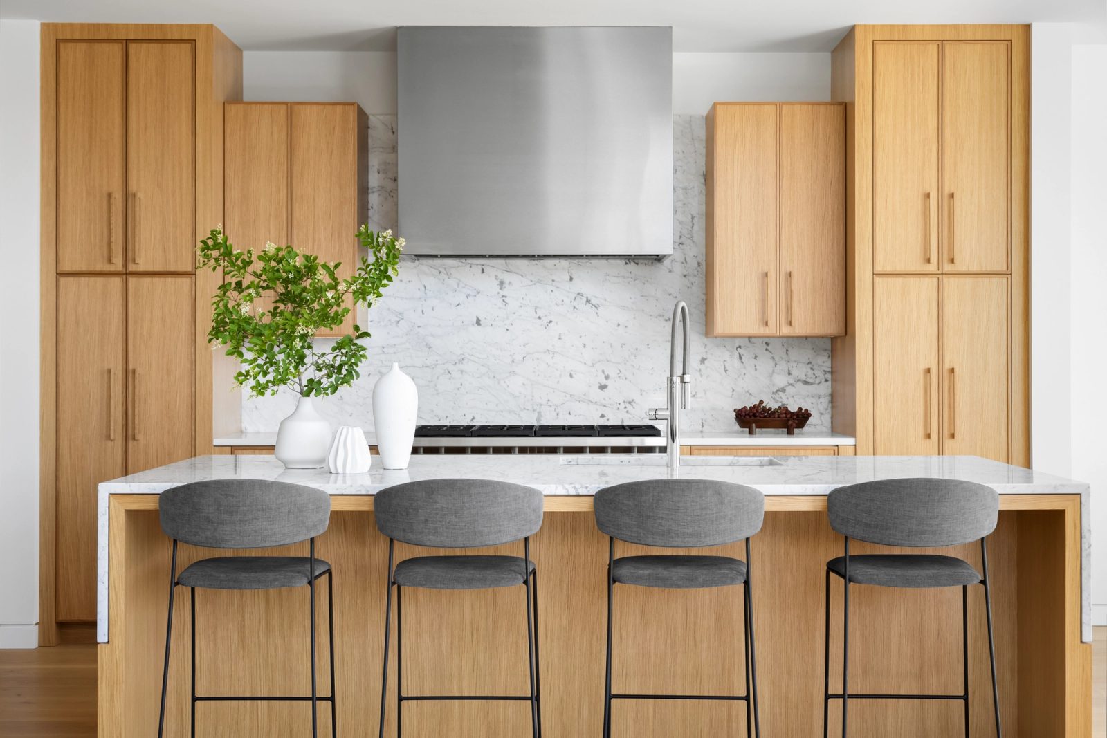 Kitchen with pale oak cabinetry to the ceiling, a marble backsplash behind the range, and four upholstered stools at a marble island.