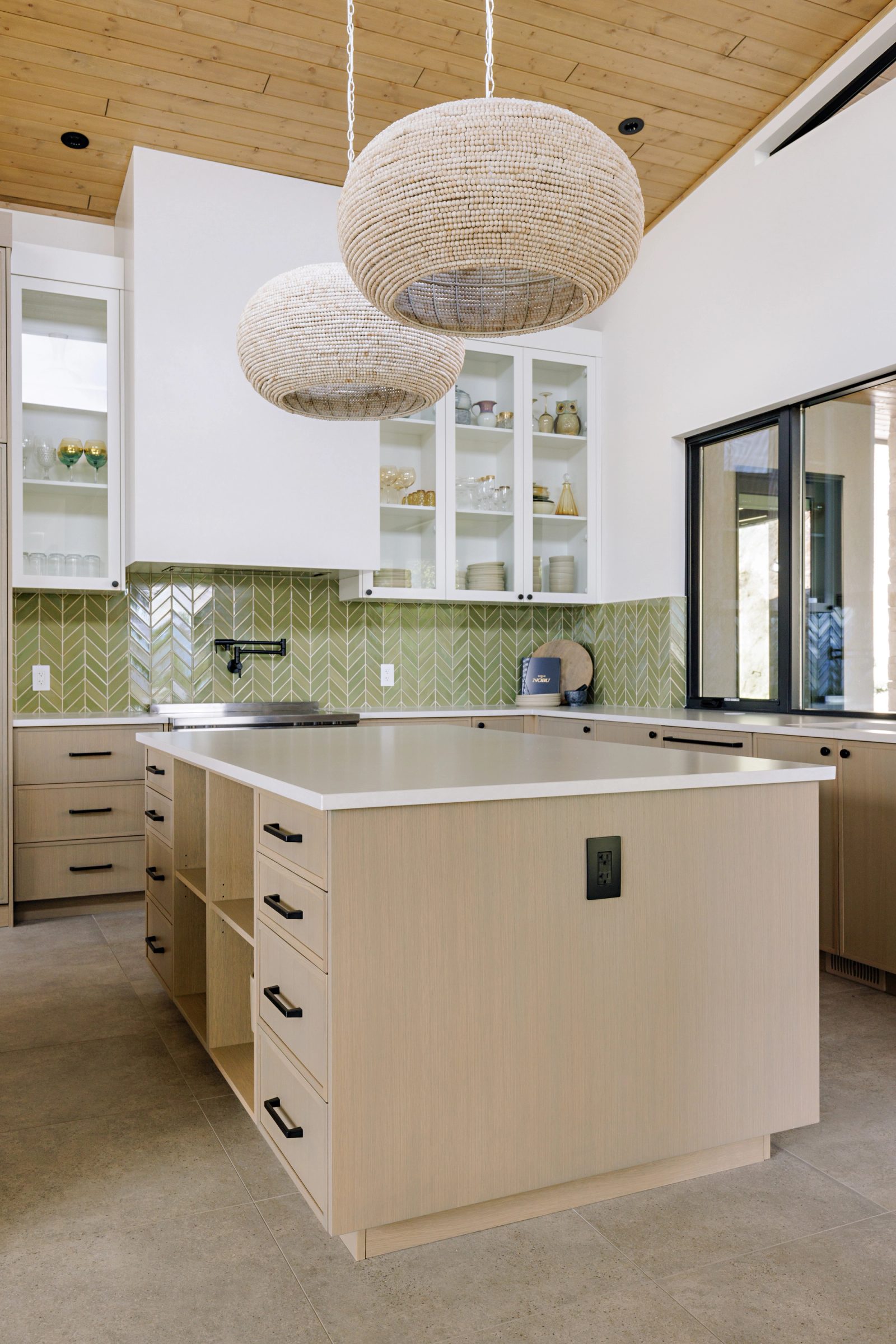 a square island in pale wood with an open shelf end, seen beneath two large beaded pendants.