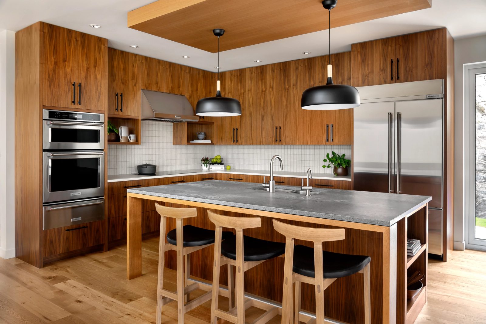 Walnut kitchen with a honed grey stone island, black pendants and a recessed timber ceiling