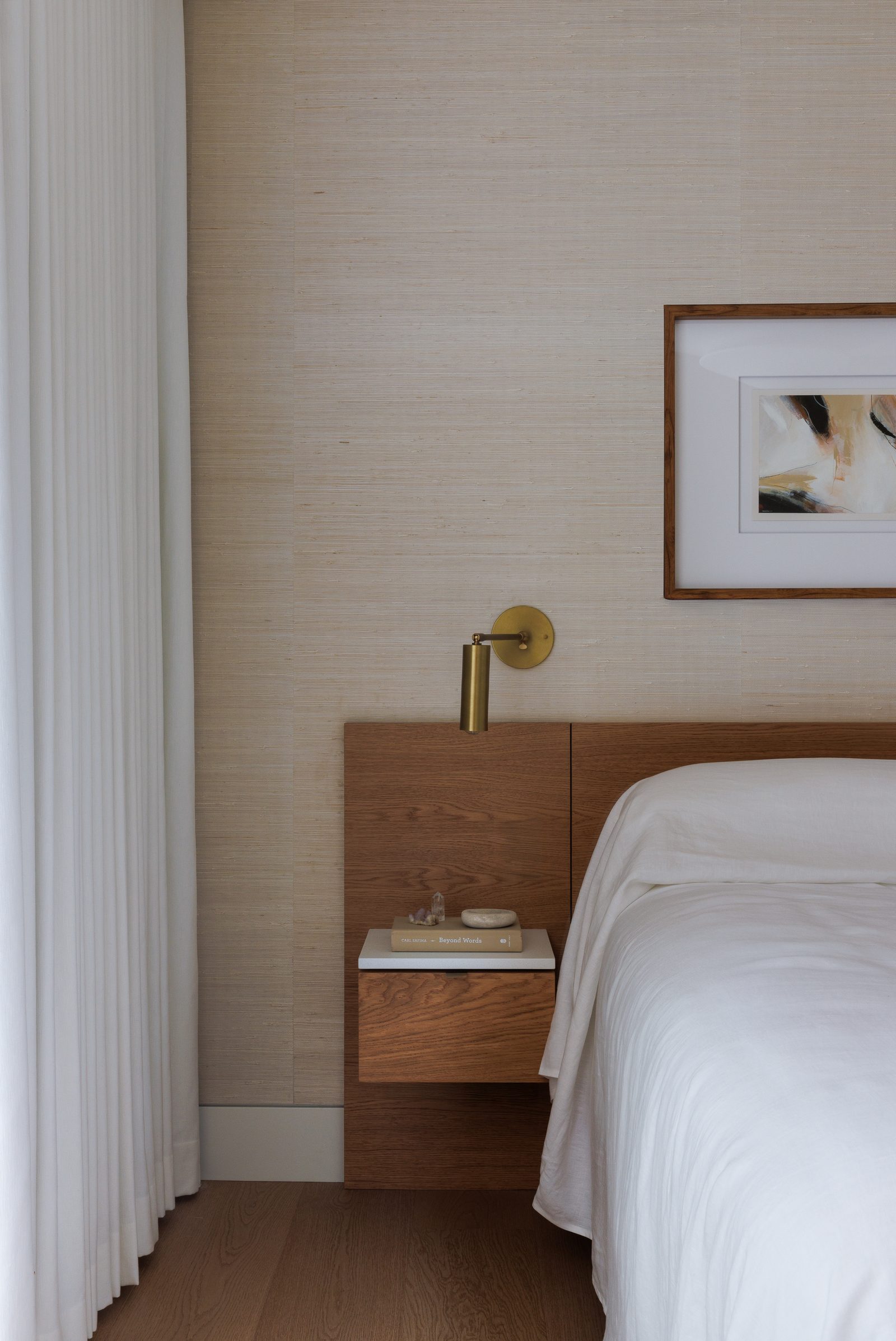 Right: a floating oak nightstand with a stone top, a brass reading light on the wall above it.