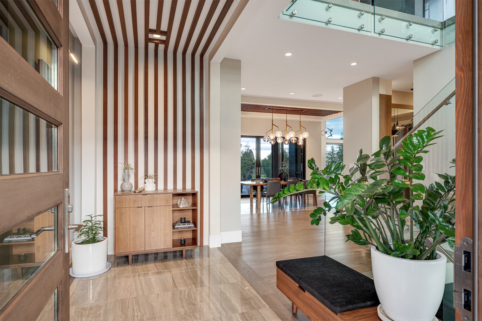 Entry hall lined with vertical walnut slats, looking through to the dining room and the trees past the glazing