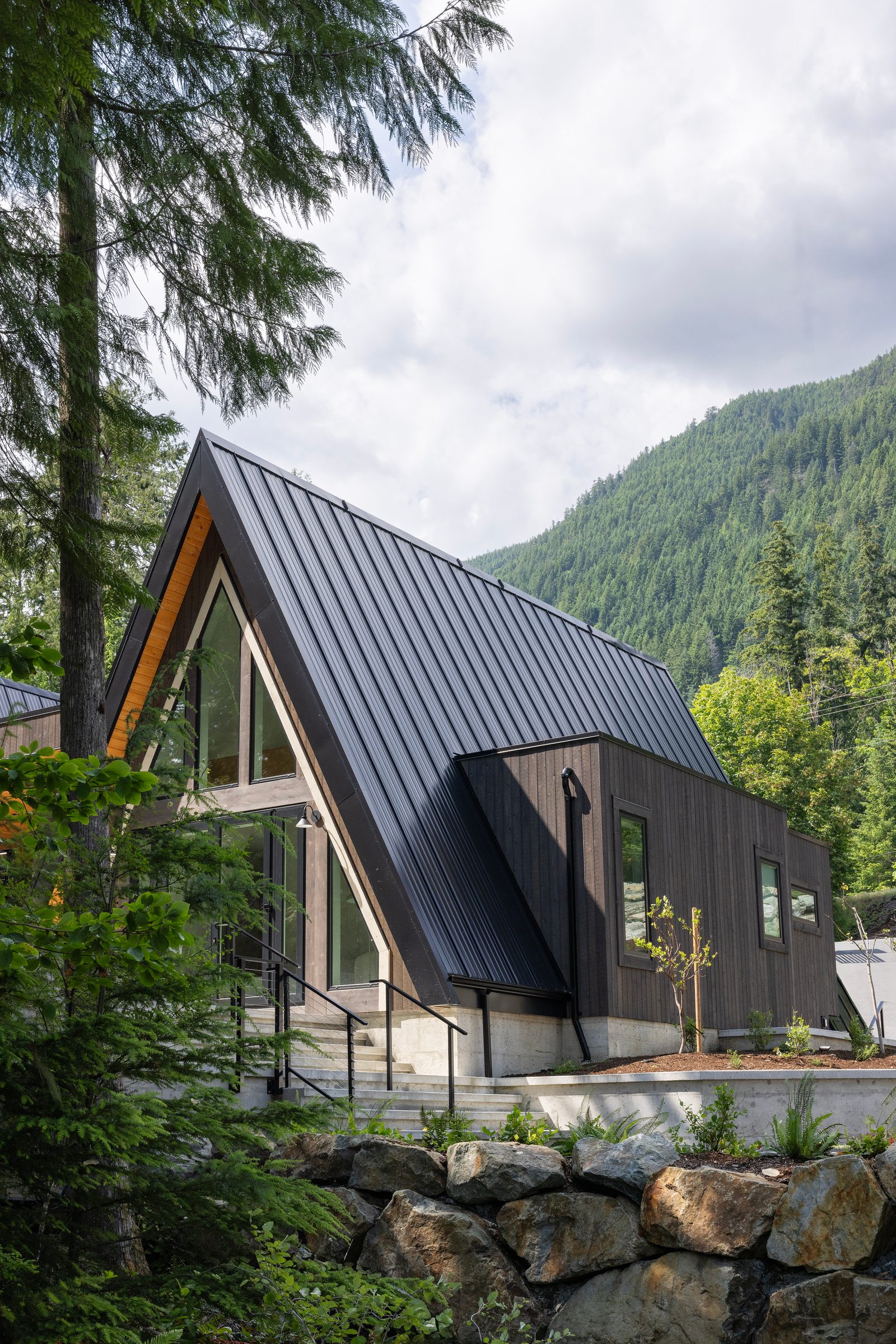 Black A-frame above a rock retaining wall with a forested mountain behind