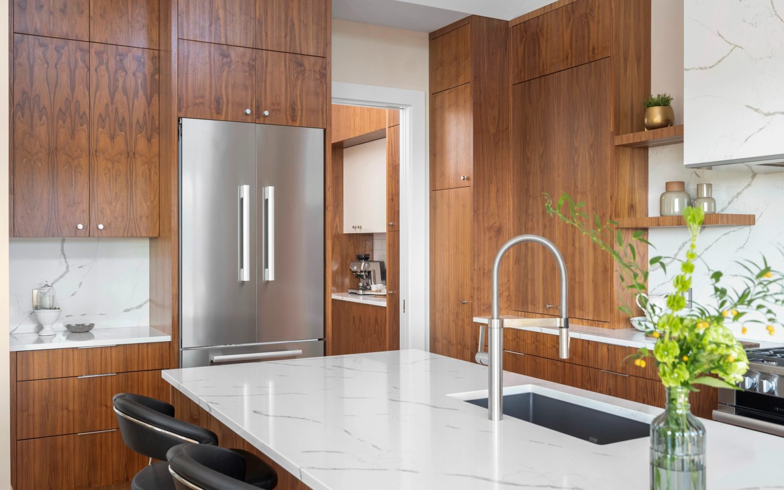 Kitchen wall in book-matched walnut with an integrated fridge and the butler pantry beyond