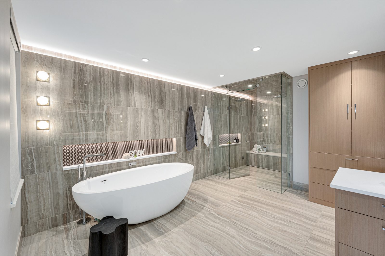 Ensuite with a freestanding tub, travertine-look tile and a glass shower with a bench