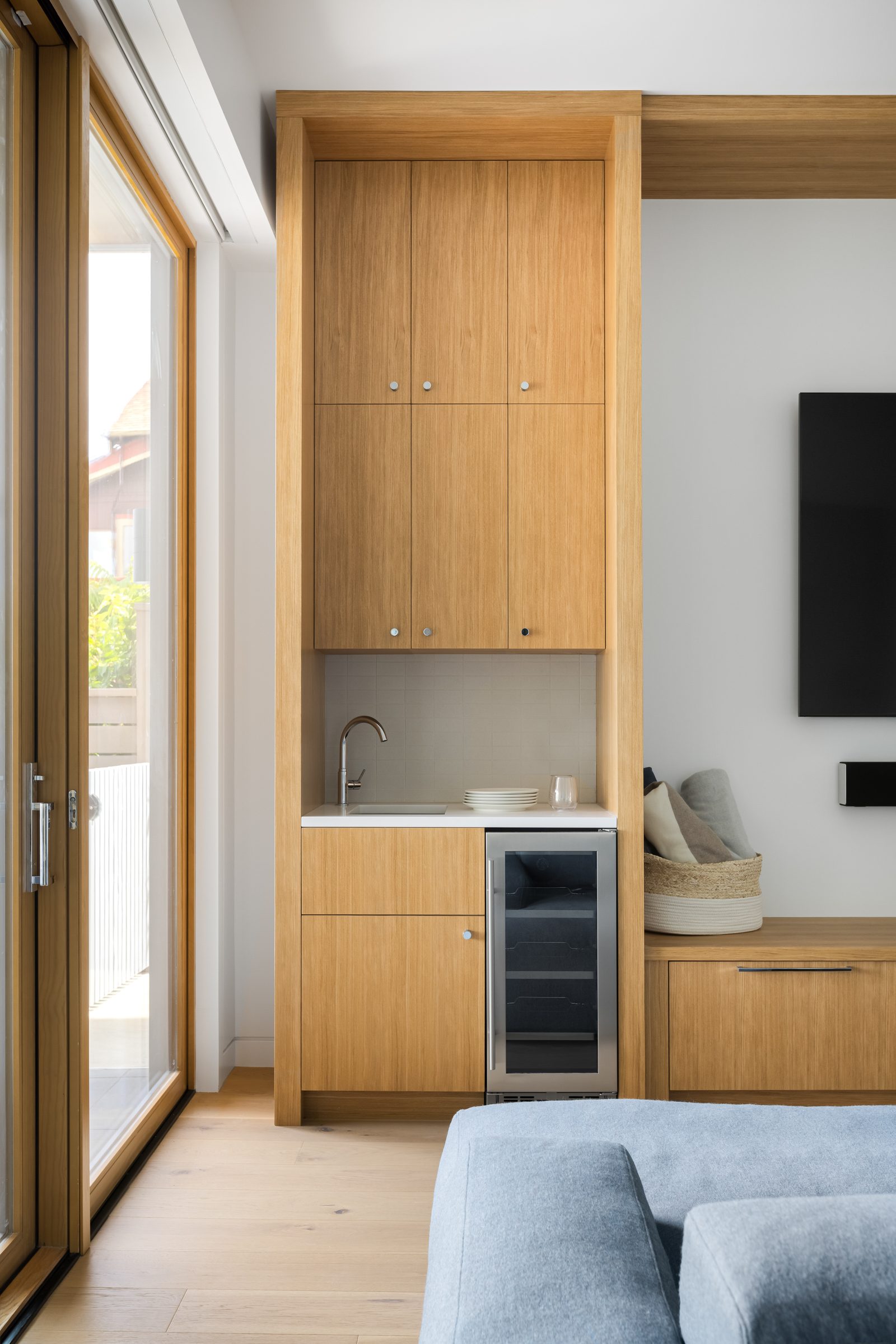 Wet bar recessed in oak joinery, with a small sink, a glass-fronted cooler and a bench seat alongside.