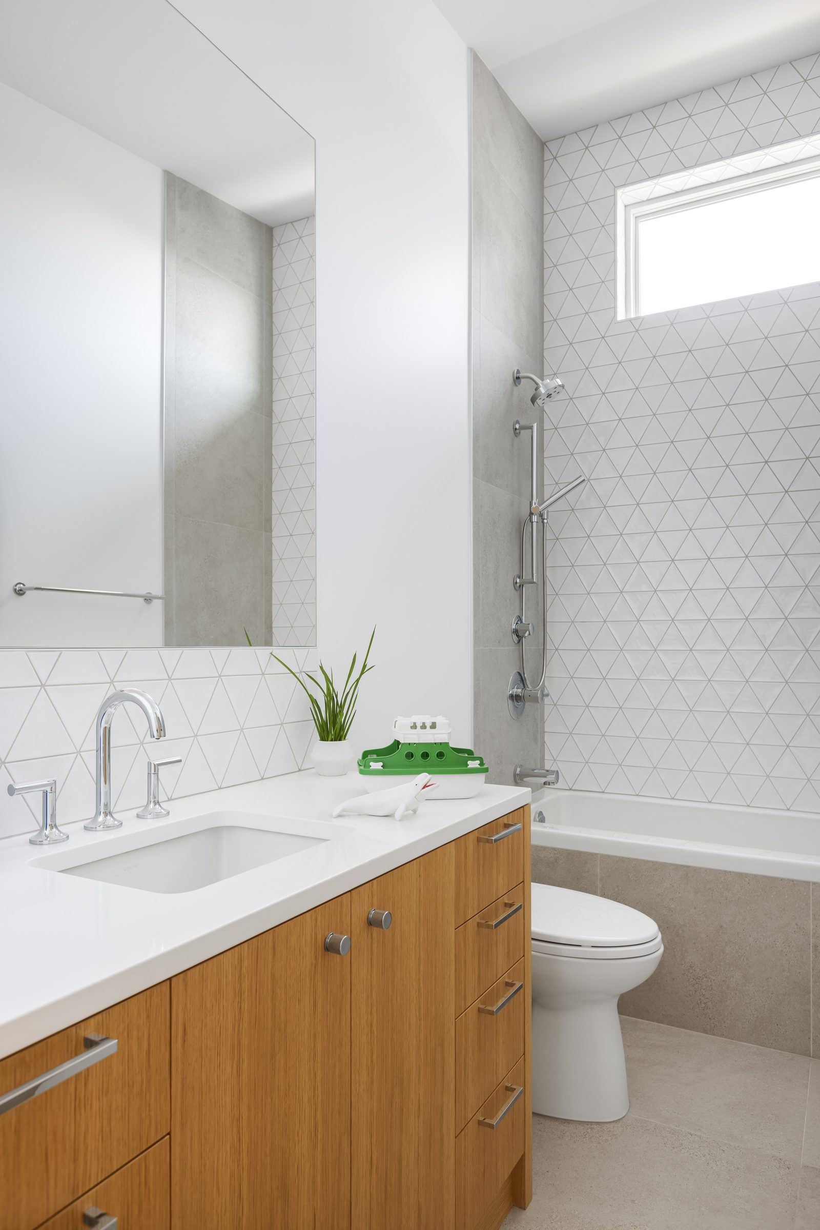Second bathroom with a white counter, triangular wall tile and a tub under a high window.