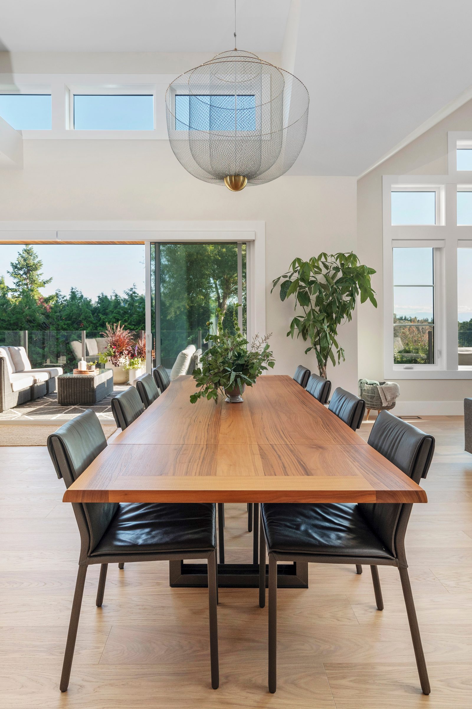 Walnut dining table for ten under a woven wire pendant, with sliding doors open to the deck