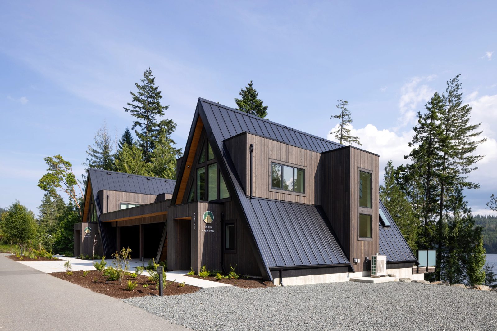Two joined A-frame cabins in dark stained cedar, the lake visible at right
