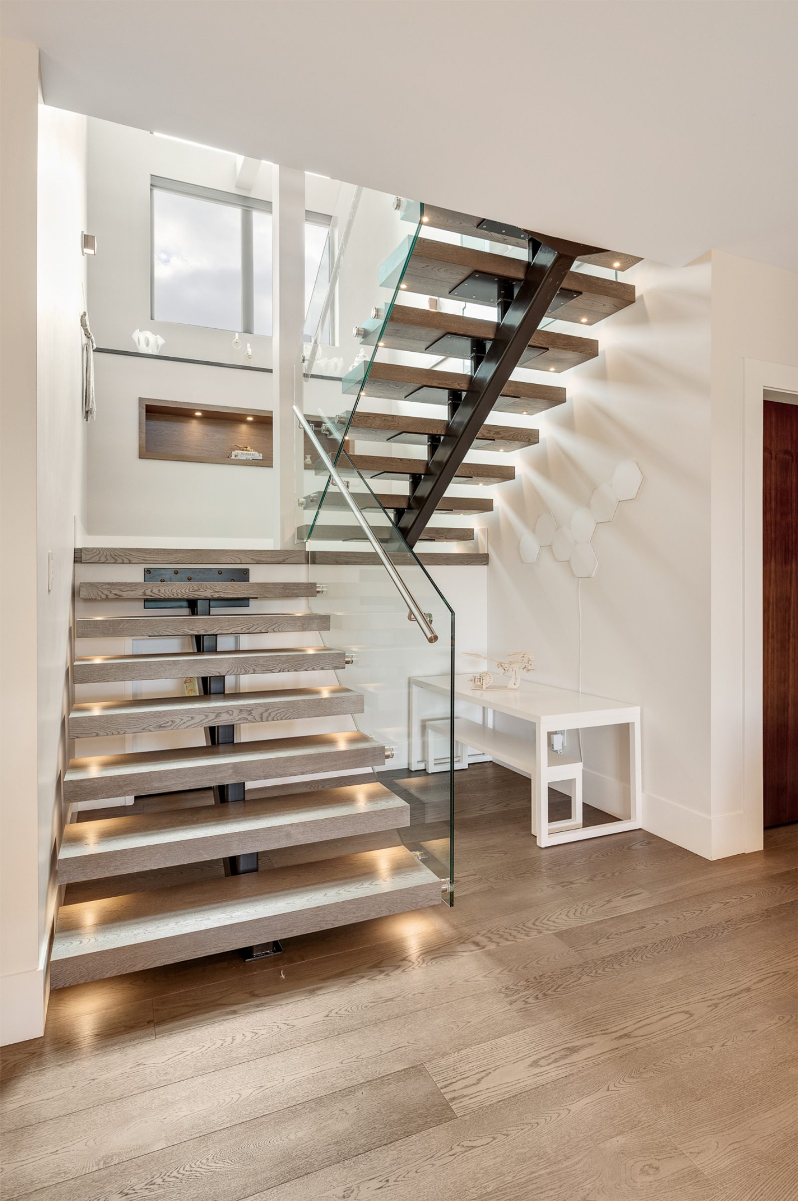 Open-riser stair treads cantilevered from a steel stringer, each tread lit from beneath