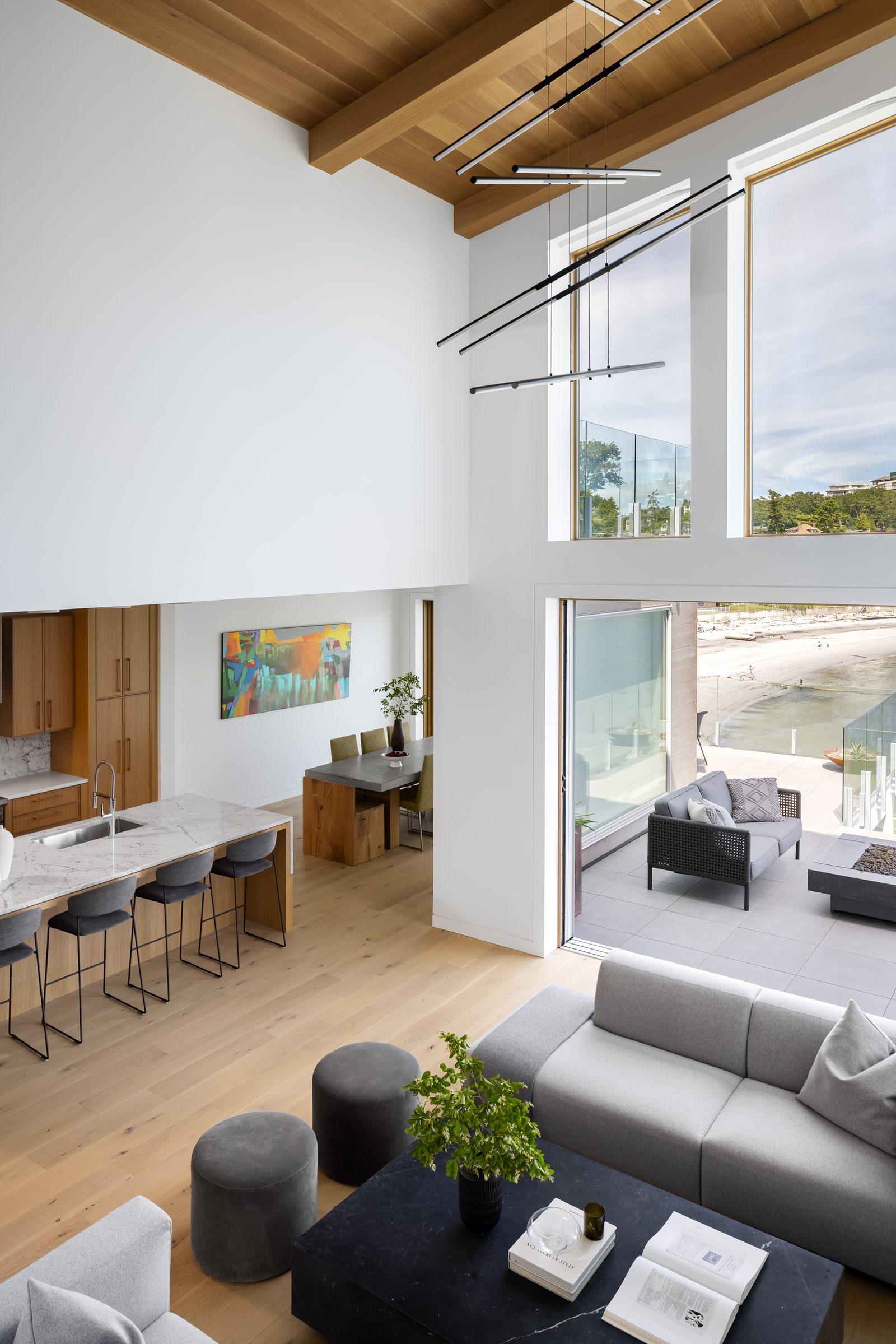 View down from the mezzanine across the living room, kitchen island and dining table to the terrace and the beach.
