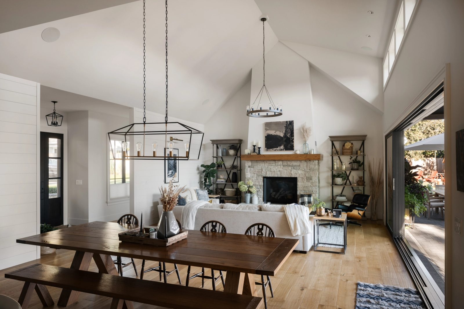 Vaulted great room with a stacked stone fireplace, timber mantel and sliding doors open to a covered patio, with a plank dining table in the foreground