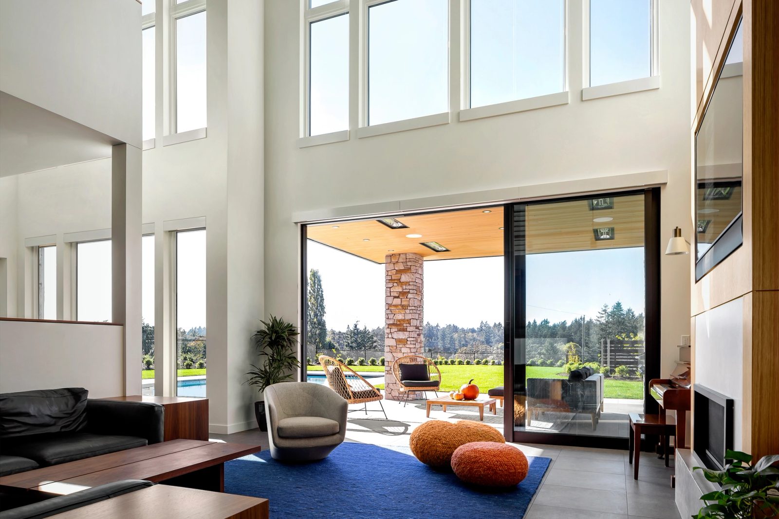 Double-height living room with a glazed wall slid open to a covered terrace and pool beyond