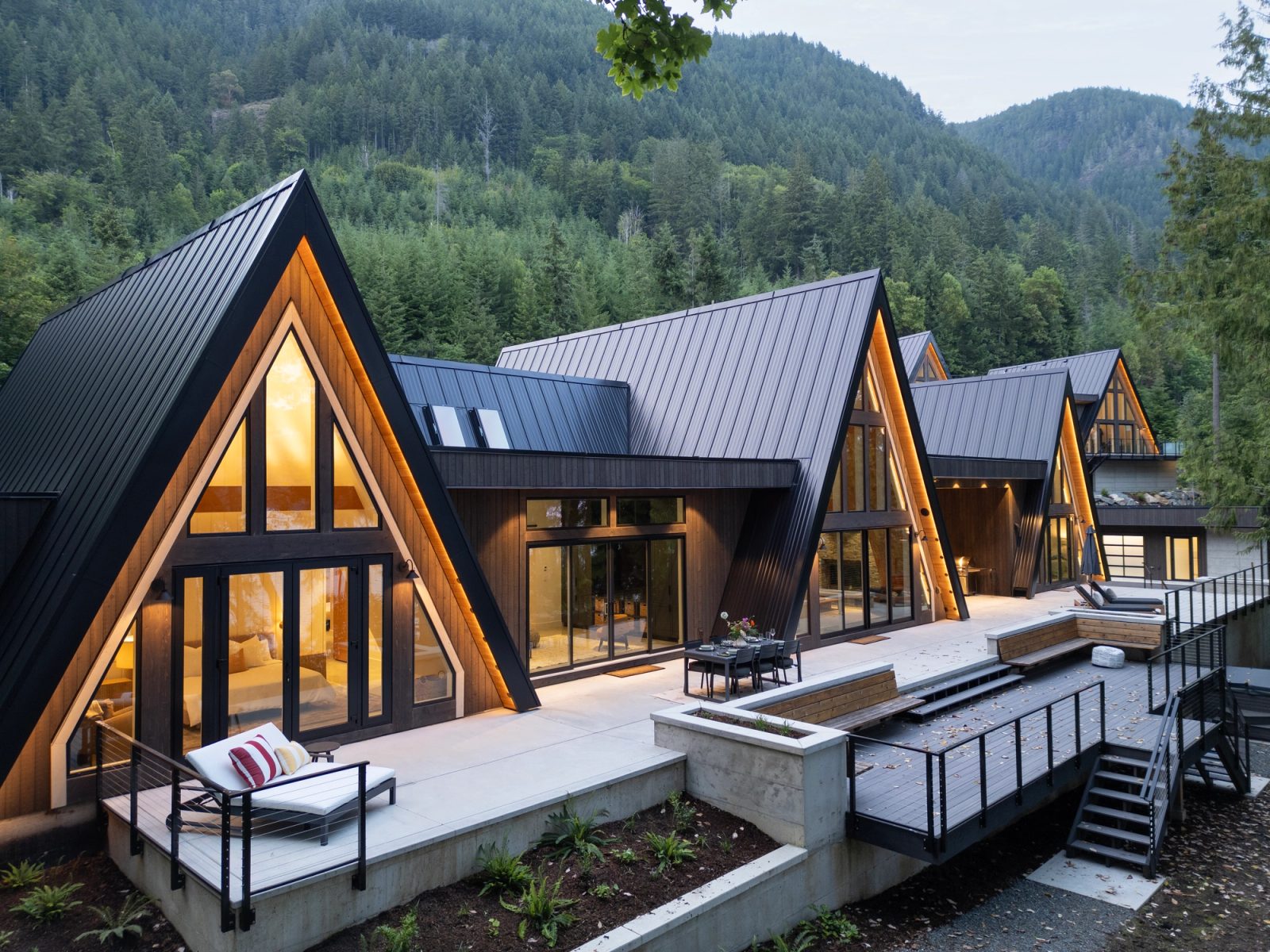 Four A-frame gables lit from within at dusk, seen from above the deck