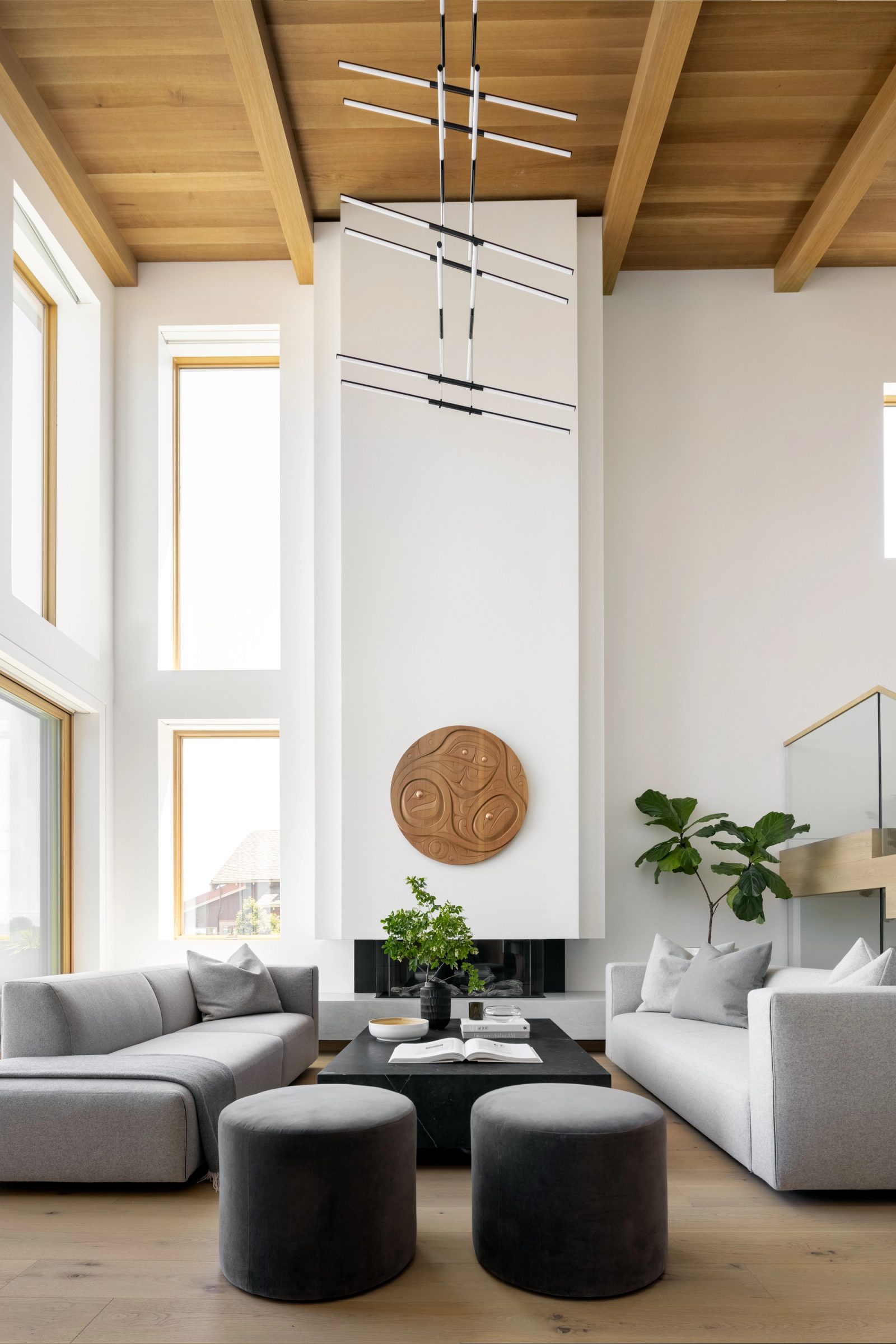 Double-height room with a plaster chimney breast, a carved cedar roundel above the firebox, and a plank ceiling on exposed beams.