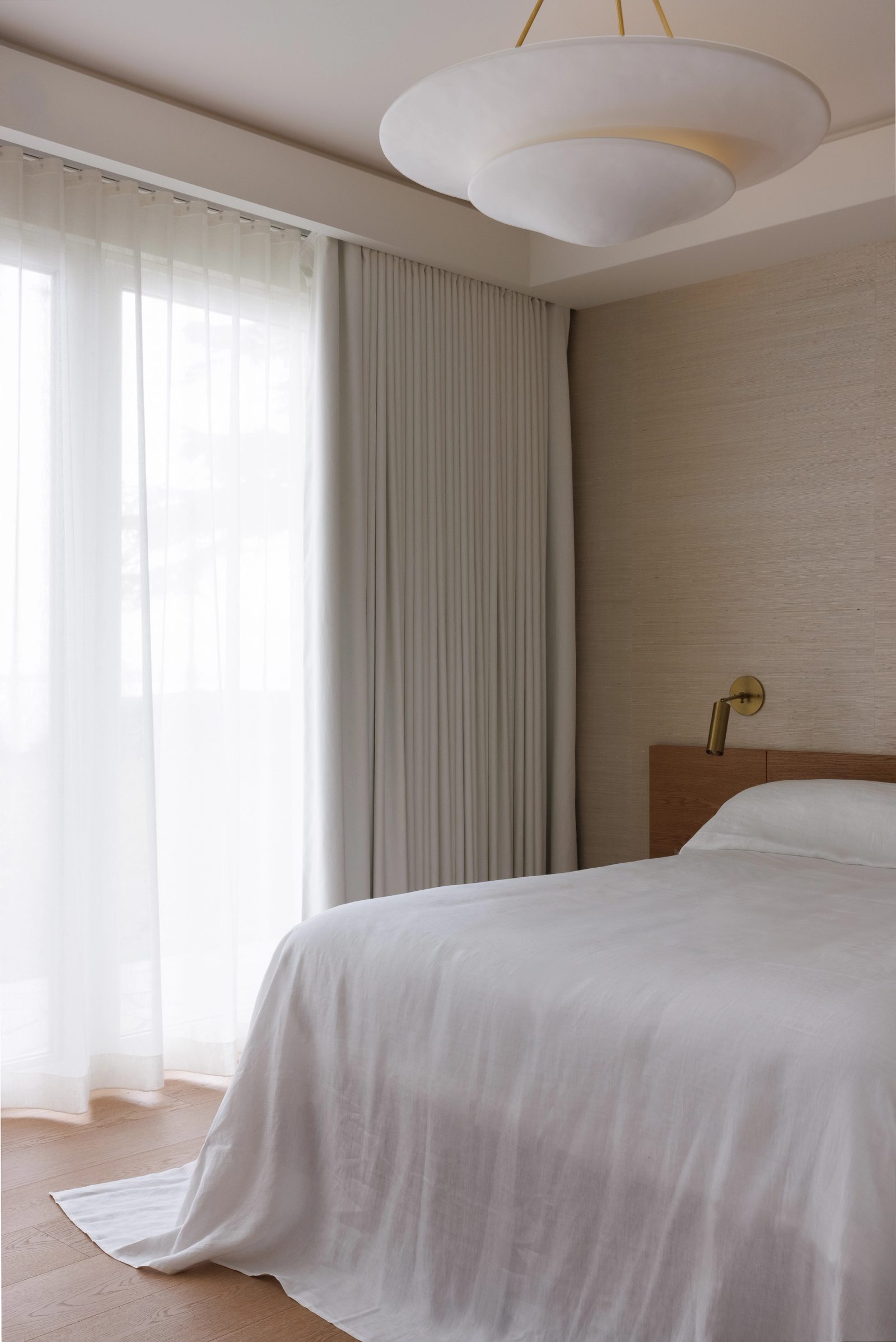 Left: a bedroom in grasscloth and sheer curtains, an oak headboard and a low disc pendant above white linen.